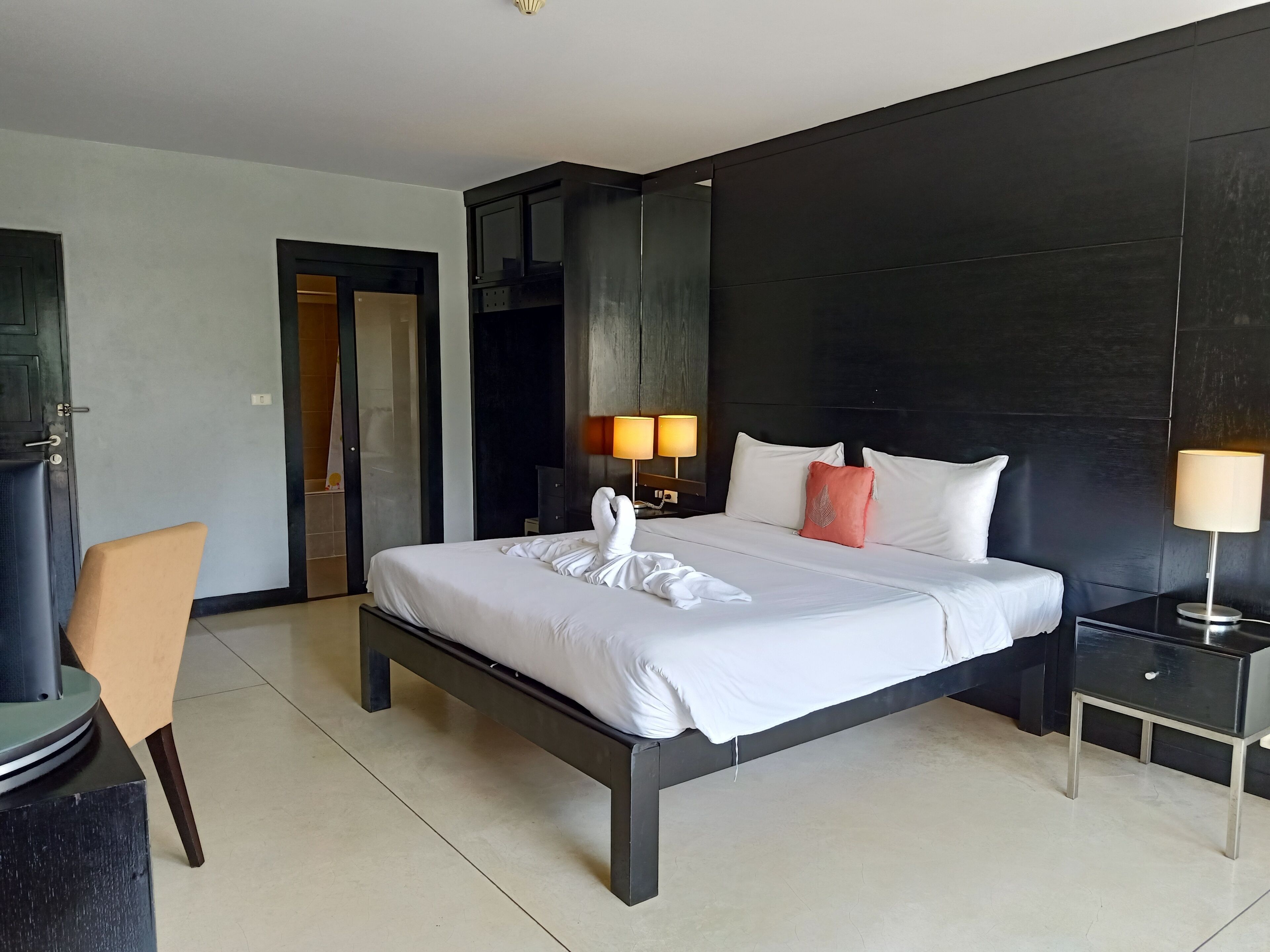 A modern hotel room with a large bed, bedside lamps, a desk, and a chair.
