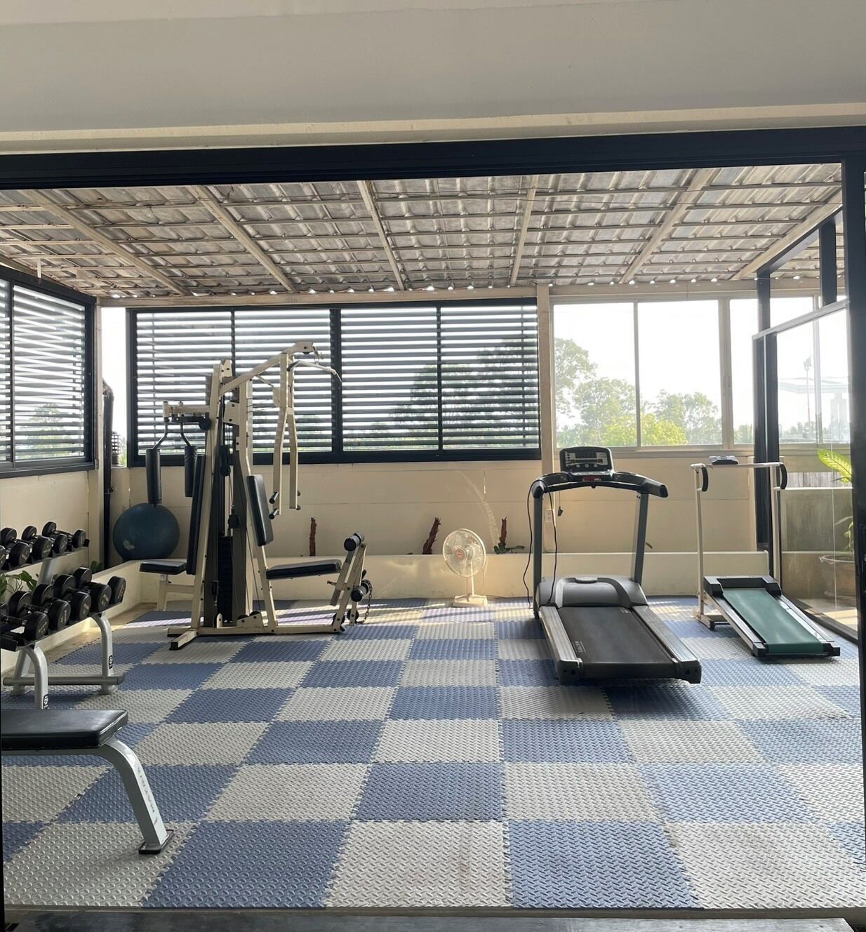 Une salle de sport équipée de matériel d’exercice, d’un tapis de course et d’un ventilateur.