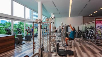 Un gimnasio con diversos equipos de ejercicio, ventanas amplias y vista a zonas verdes.
