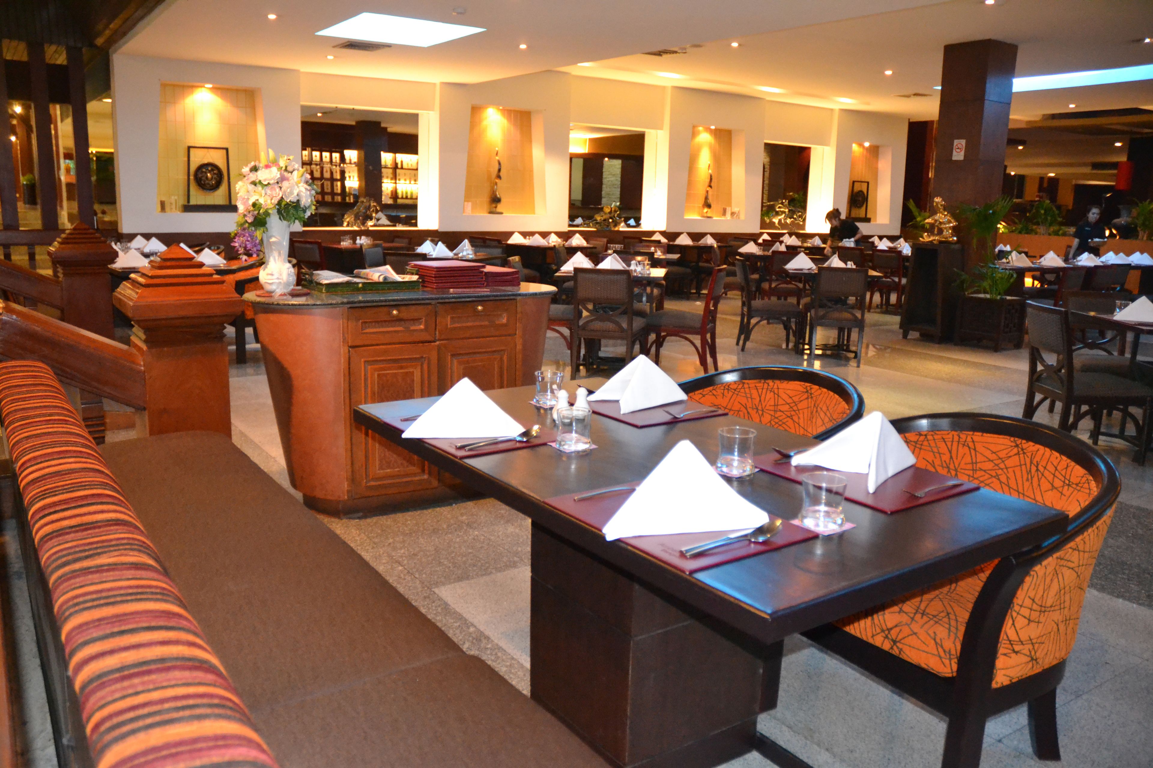 Un vaste espace de restauration dans l’hôtel, comprenant de nombreuses tables et chaises, un bar central et un coin salon avec un canapé.