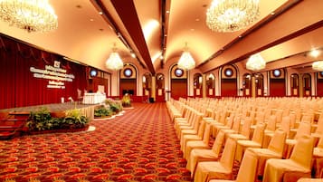Un salón amplio con filas de sillas y un escenario con cortina roja.