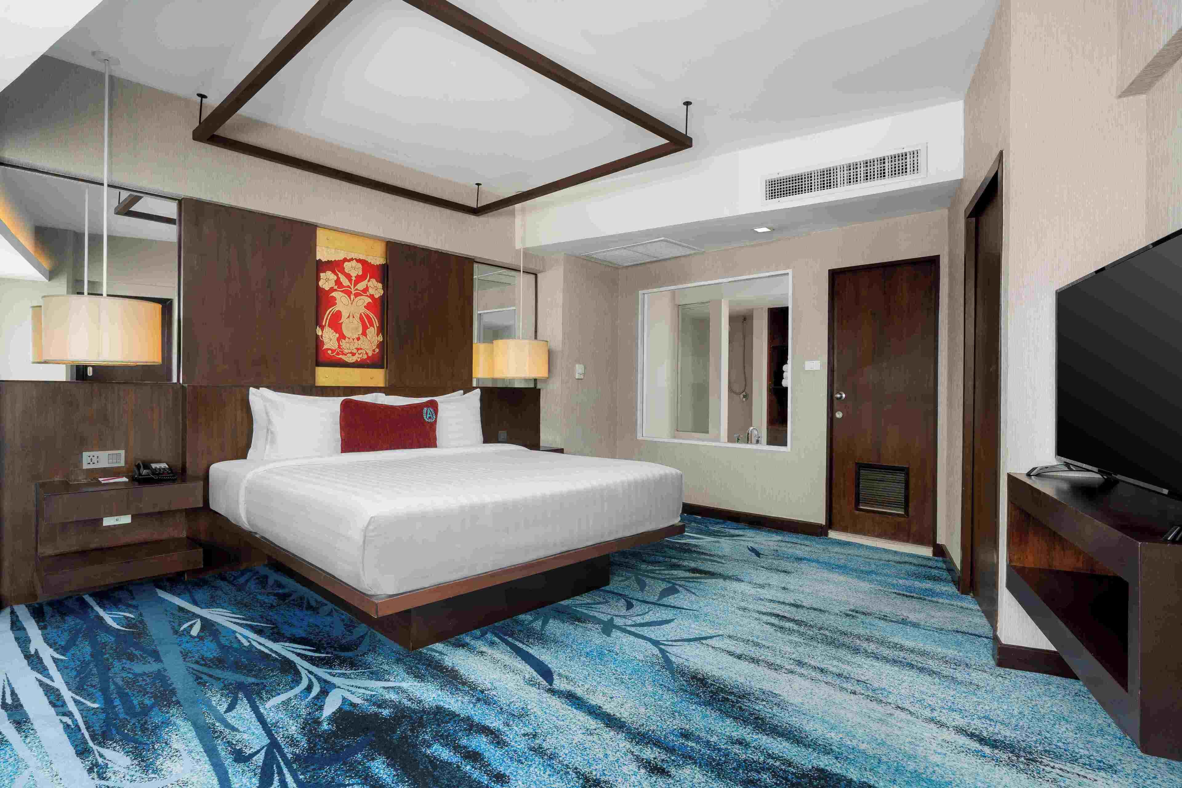 A hotel room with a large bed, a television, a desk with a lamp, and a bathroom visible through the door.