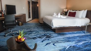 Una habitación de hotel con una cama, un escritorio con computadora, un televisor y un frutero.