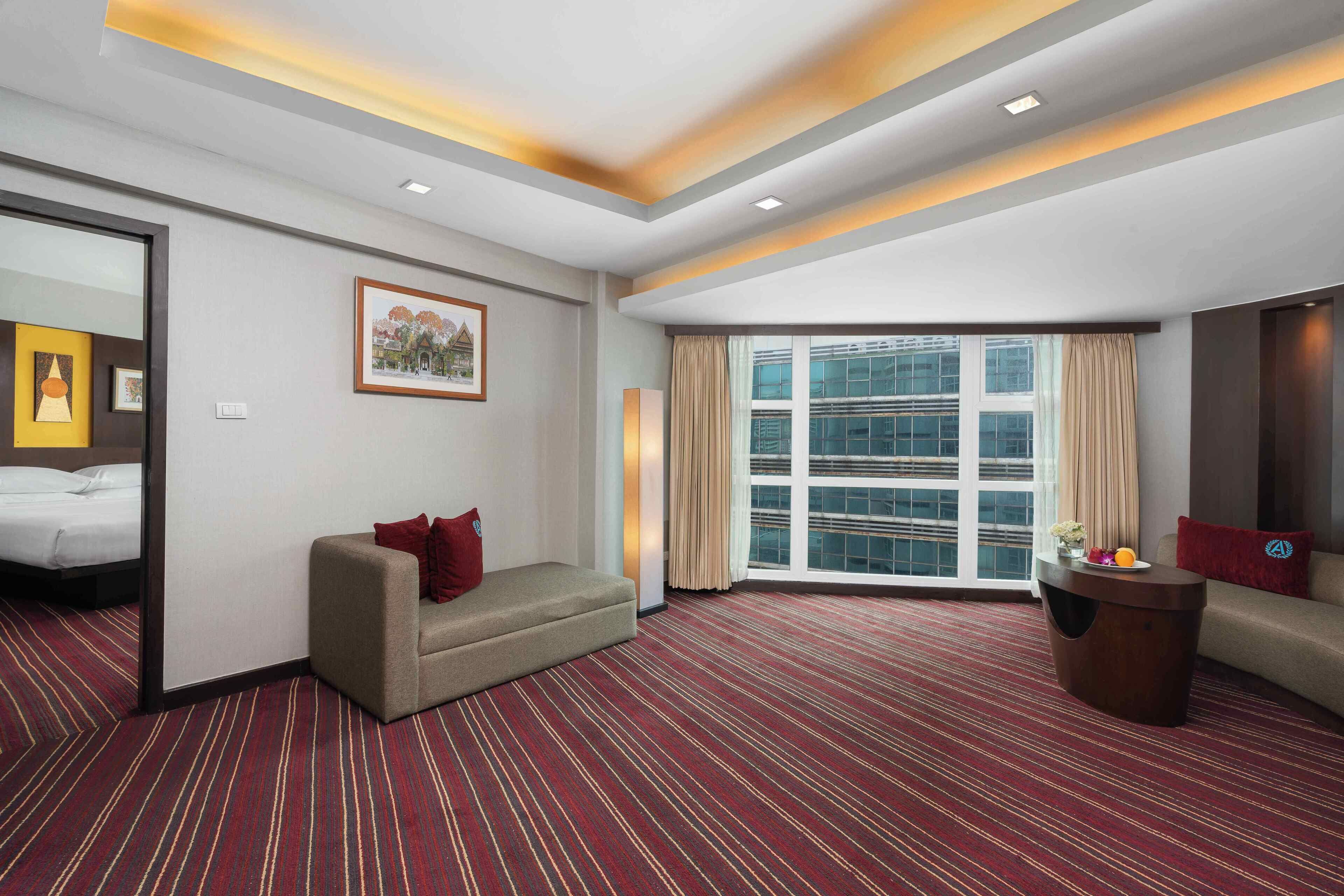 Habitación de hotel con un ventanal grande, un sofá, una cama y piso alfombrado.