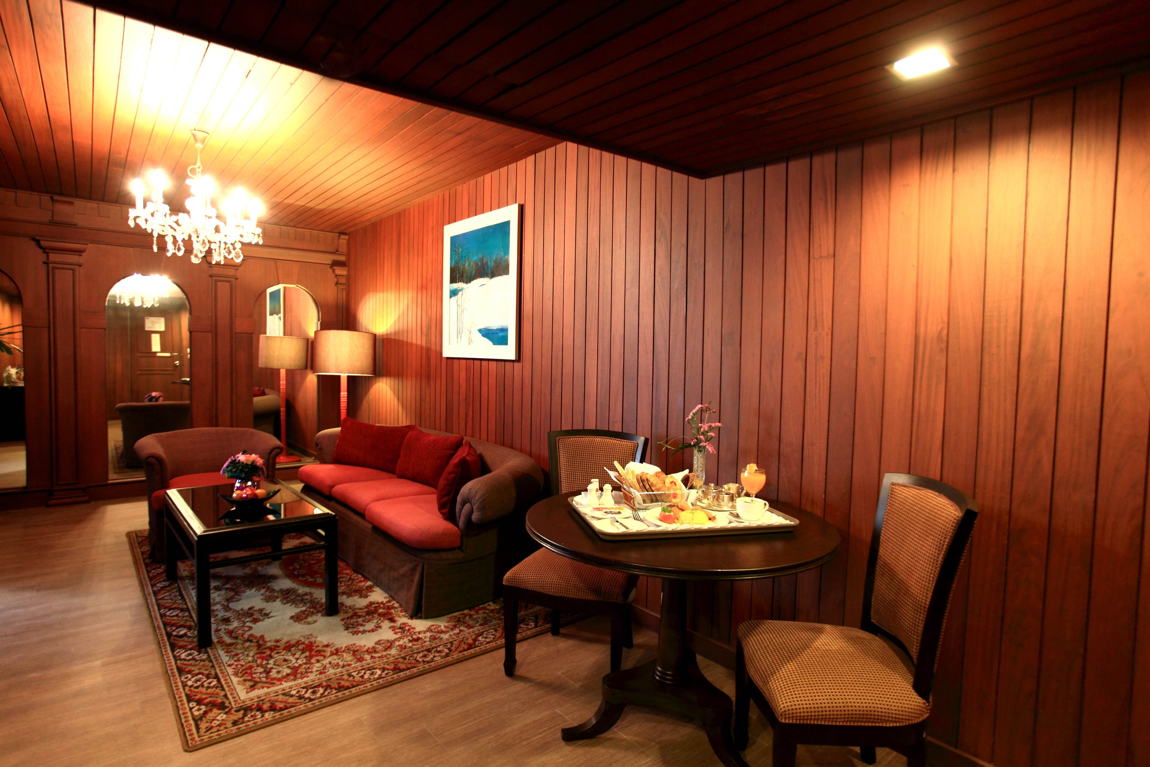 A cozy room with a wooden paneled wall, a red sofa, a dining table with chairs, and a chandelier.