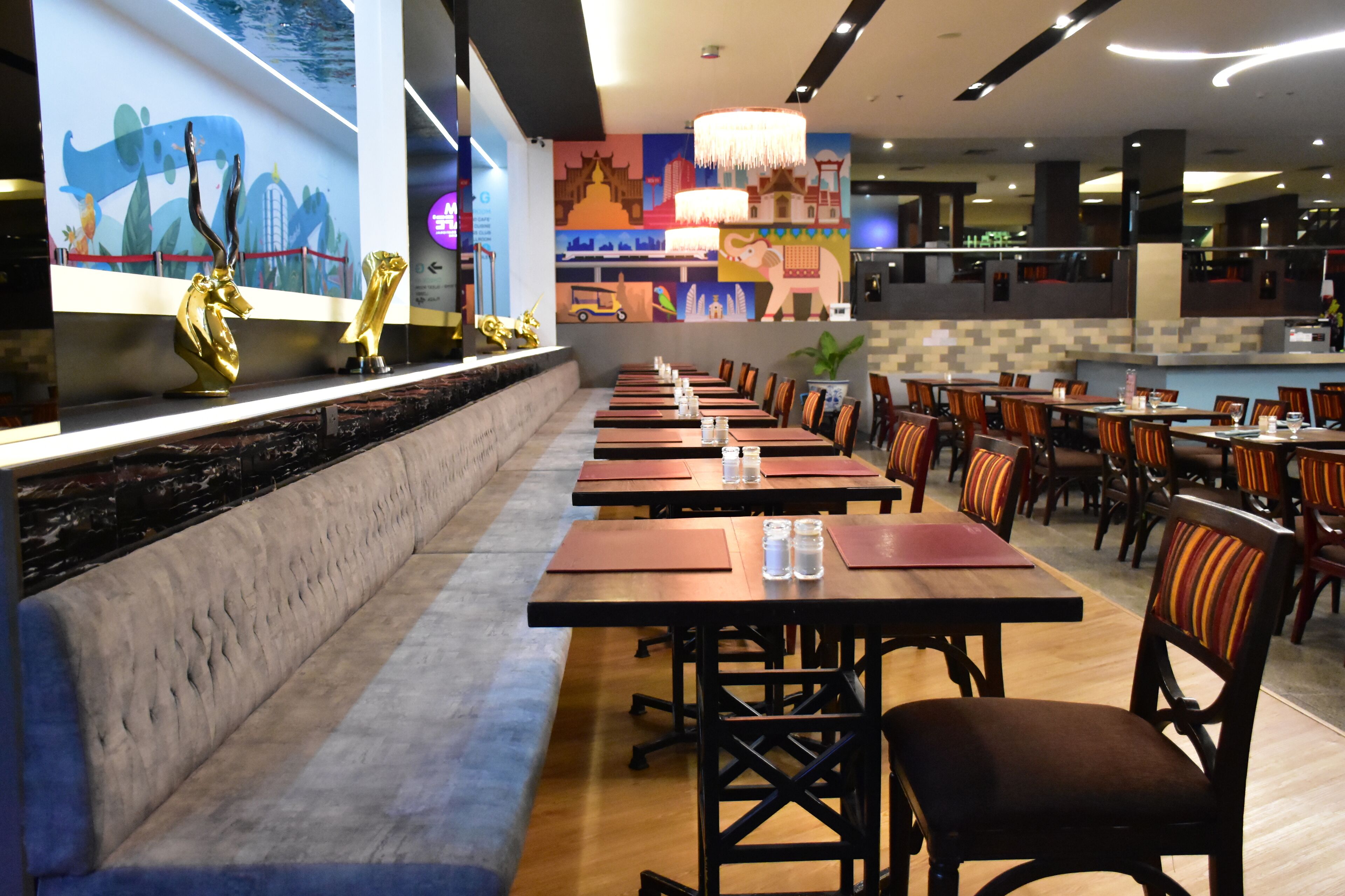 A restaurant with long tables and chairs, a cushioned bench, and a mural on the wall.