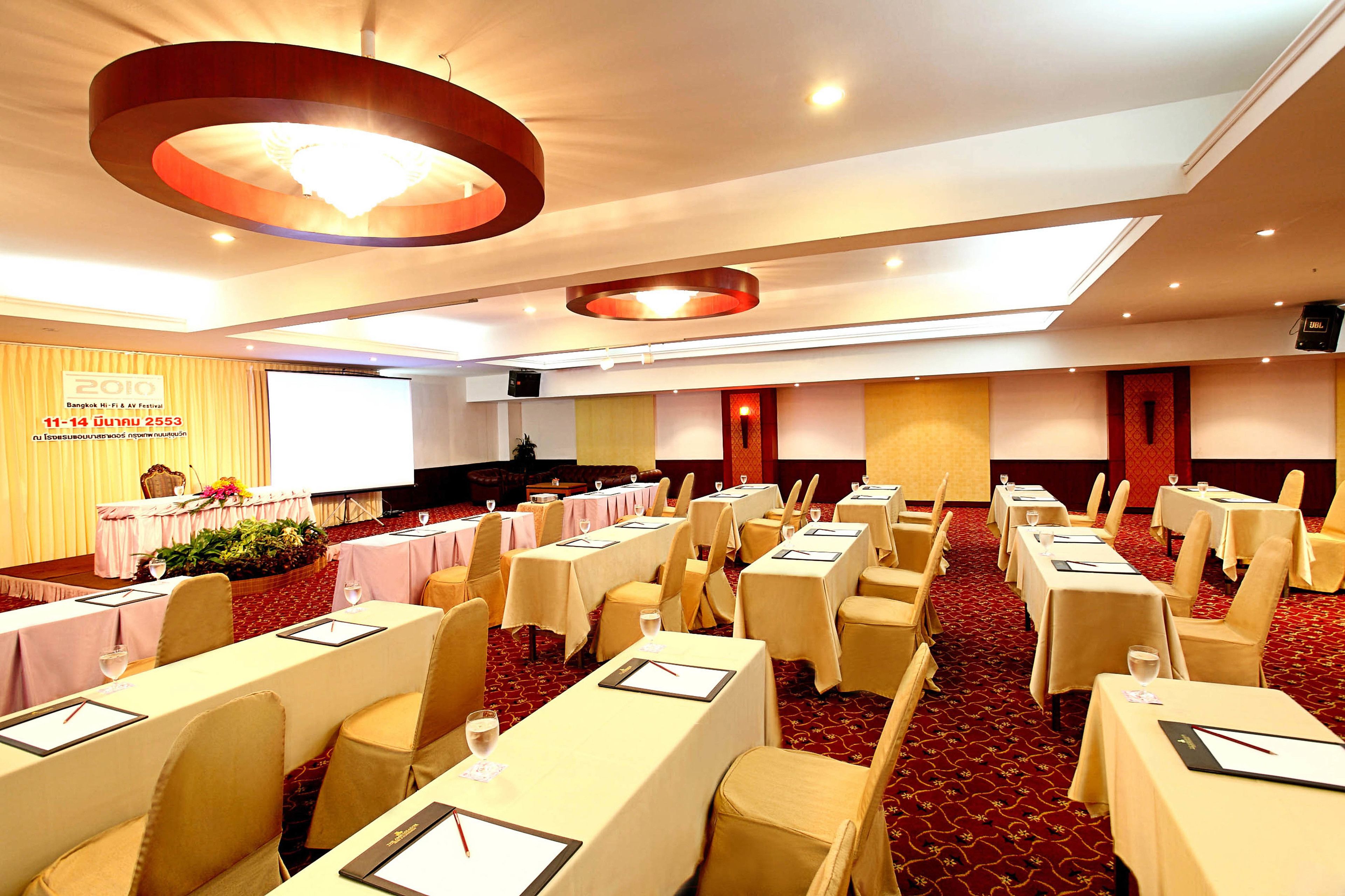 Un salón de conferencias con mesas, sillas y una pantalla para presentaciones.