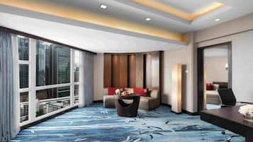 A hotel room with a large window, a sofa, a small table with a vase, and a desk with a chair.