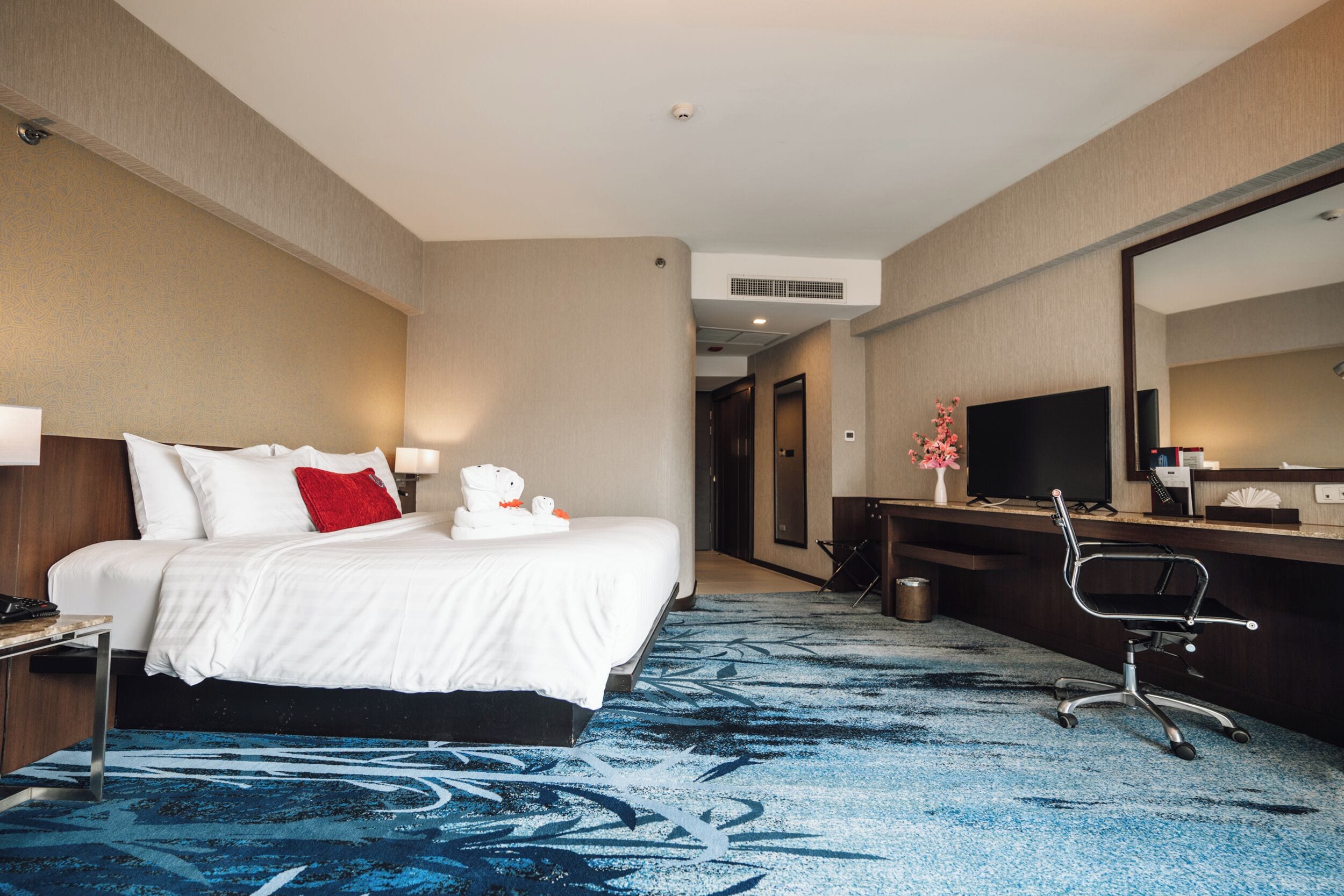 Une chambre d’hôtel avec un lit, un bureau, une chaise, une télévision et, au fond, une salle de bain.
