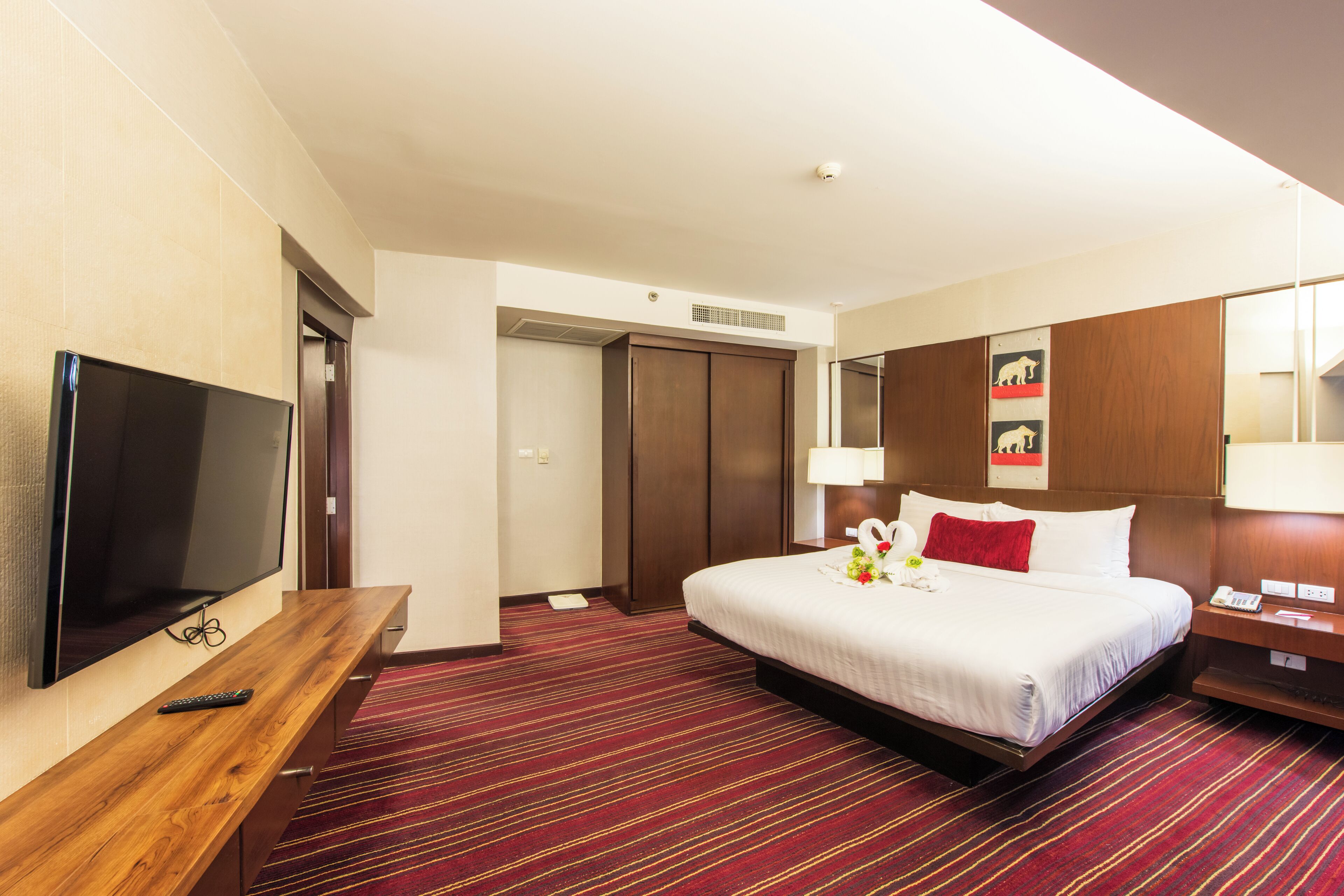 Habitación de hotel con cama, televisor, escritorio de madera, espejo y puerta.