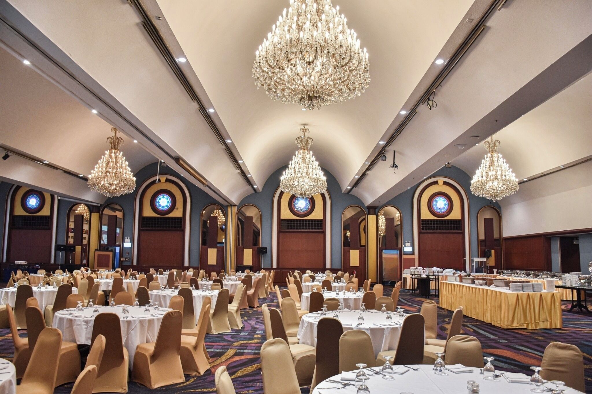 A banquet hall with round tables, banquet chairs, and large chandeliers.