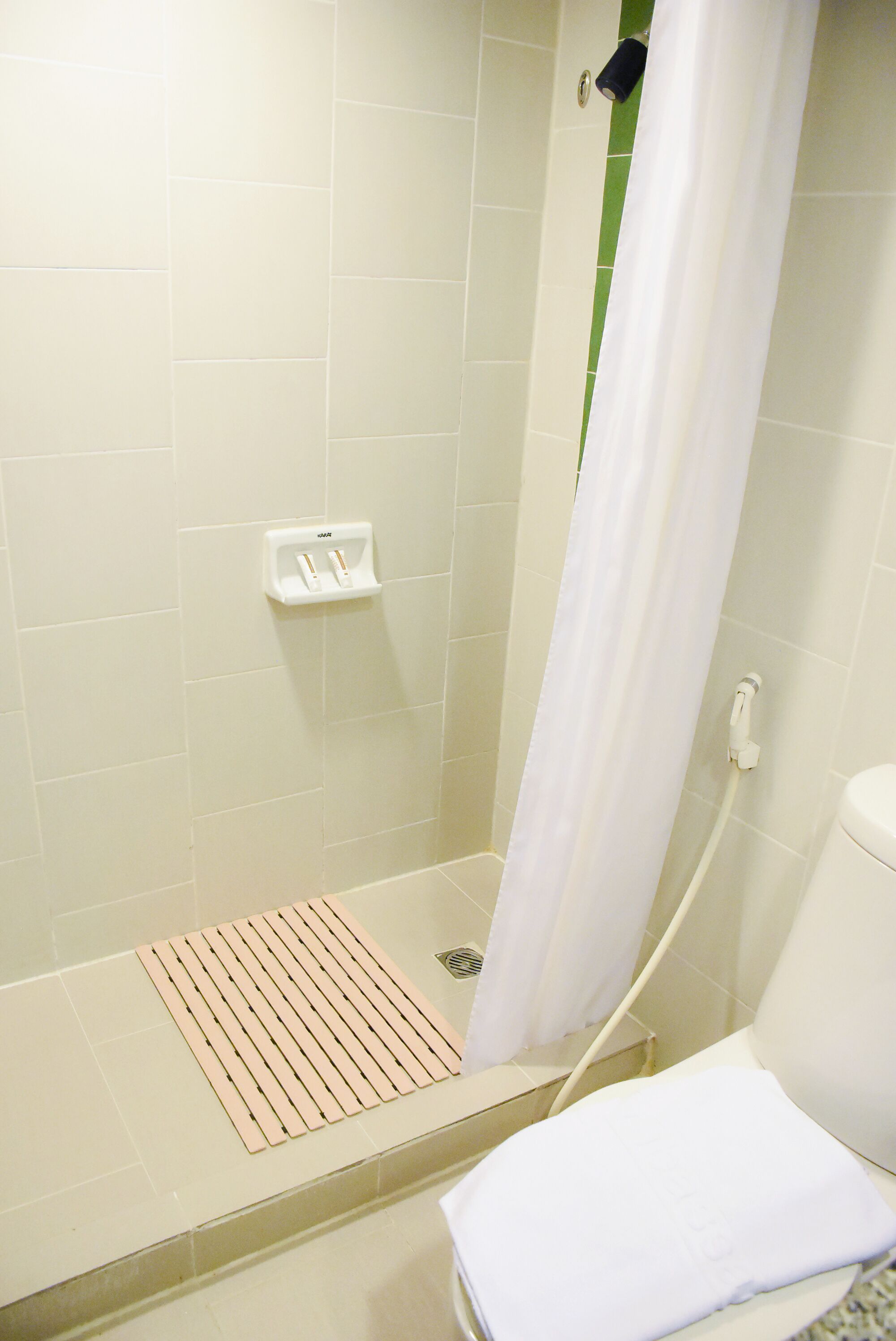A shower area with a white shower curtain, a white towel, and a white soap dispenser on the wall.