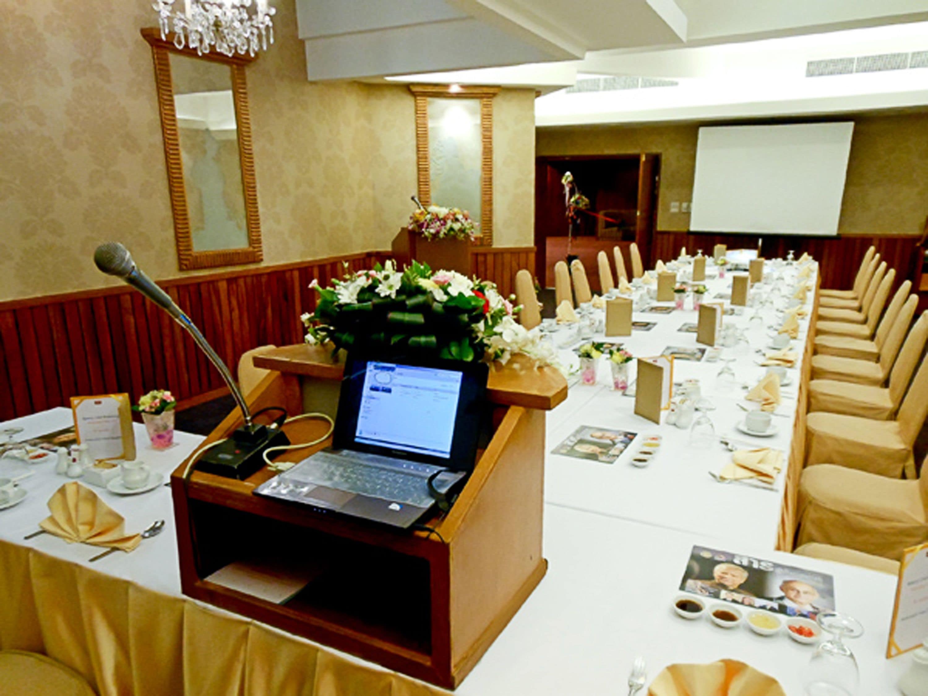 A conference room with a long table set for a meeting, a podium with a laptop, and a microphone.