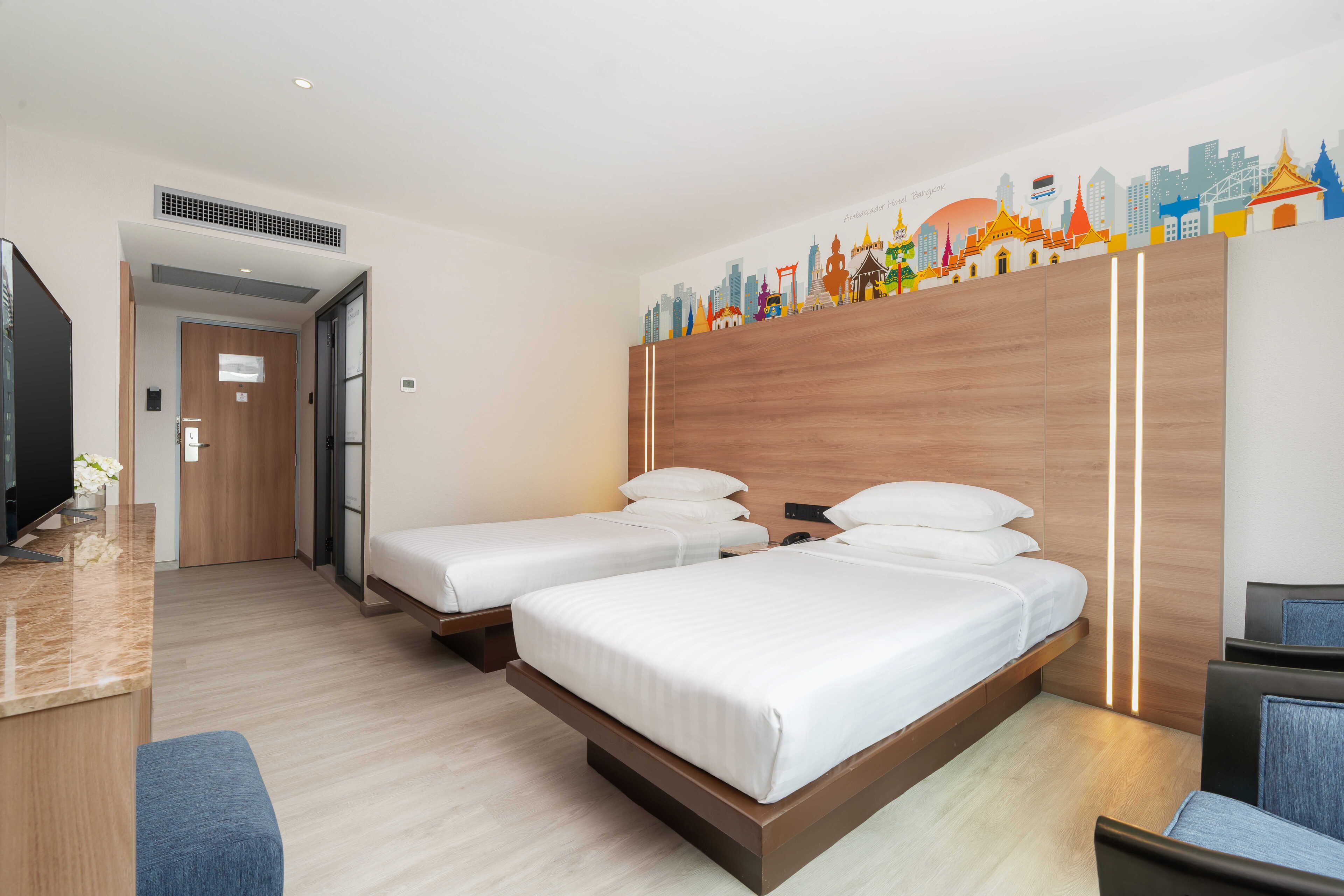 A hotel room with two beds, a TV, and a cityscape mural on the wall.