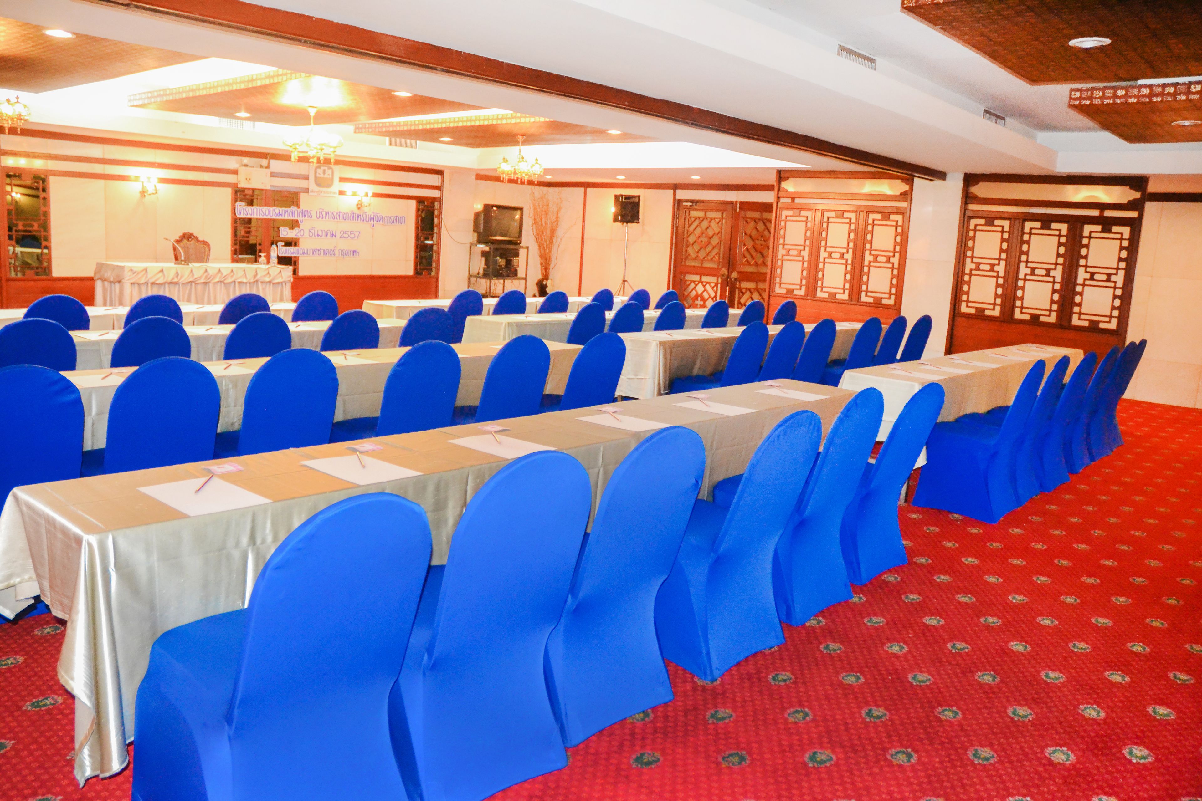 A conference room with rows of tables, blue chairs, and a red carpeted floor.