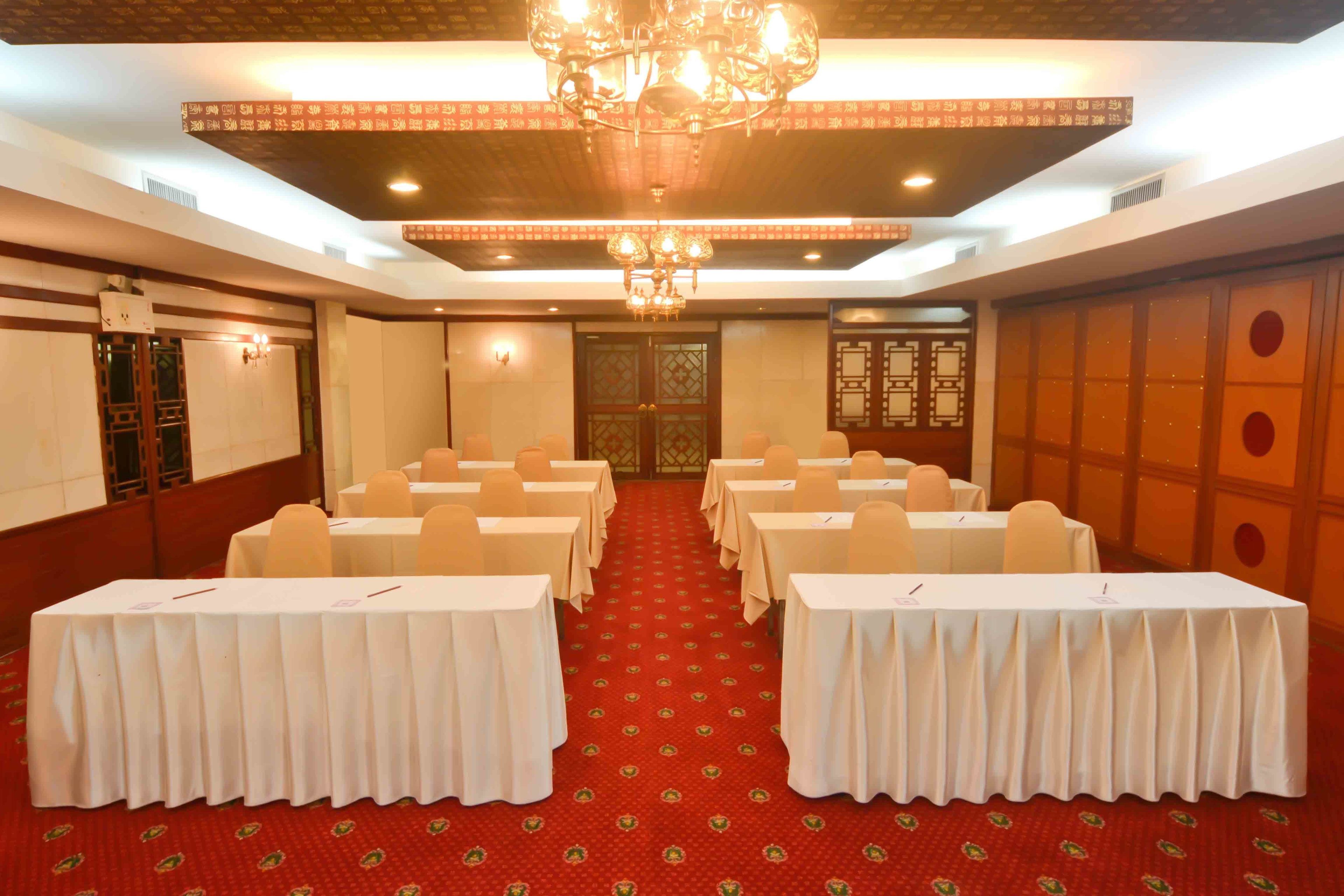 A conference room with tables set up for a meeting, a red carpet, and a chandelier.