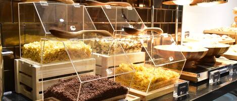 A dessert display with various types of cakes and pastries in clear containers, each labeled with its name.