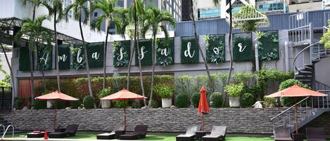 A hotel pool area with lounge chairs, umbrellas, and a stone wall with greenery.