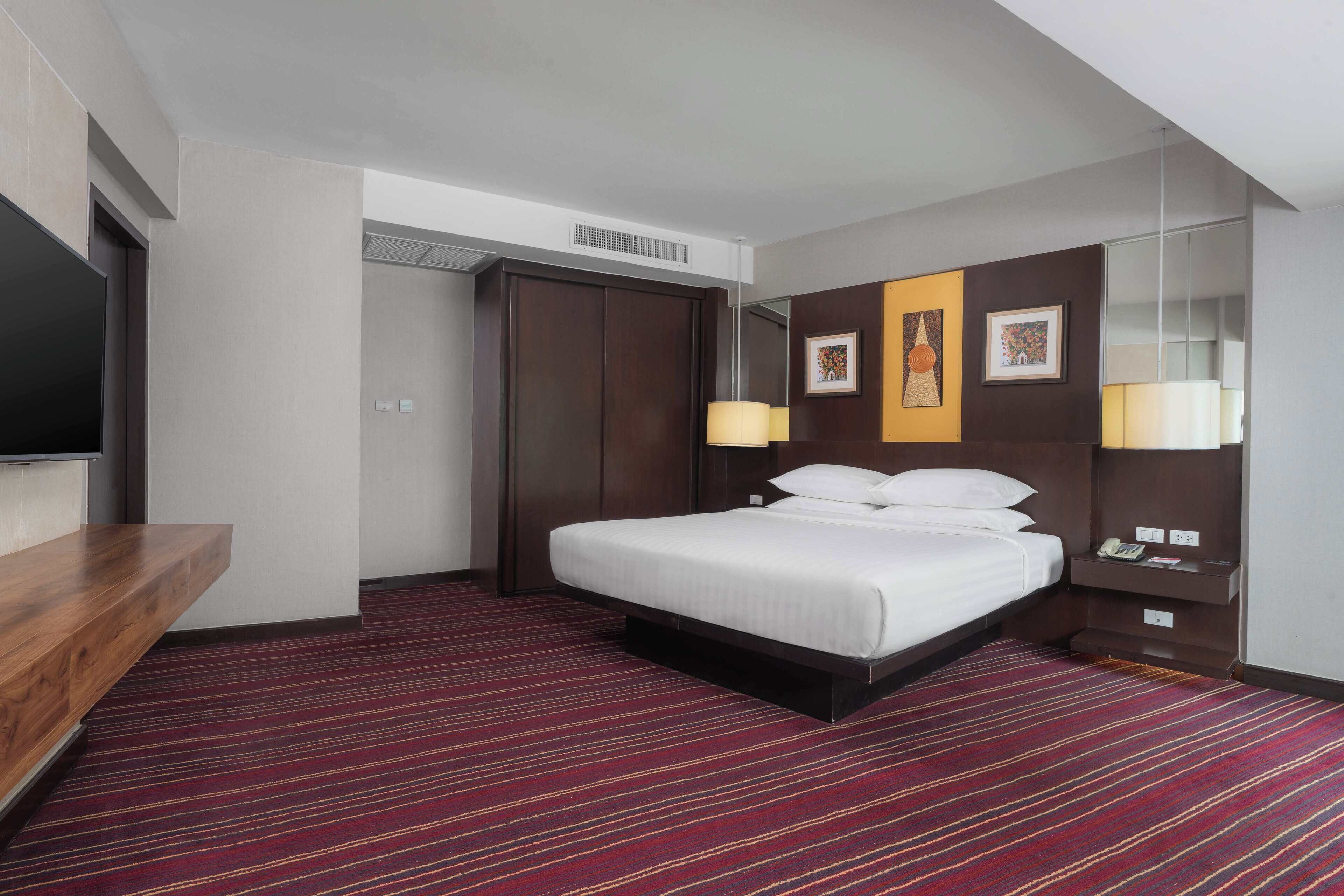 Habitación de hotel con cama, escritorio, televisor de pantalla plana, armario y espejo.
