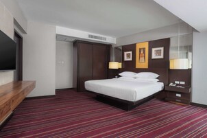 Quarto de hotel com cama, escrivaninha, TV de tela plana, guarda-roupa e espelho.