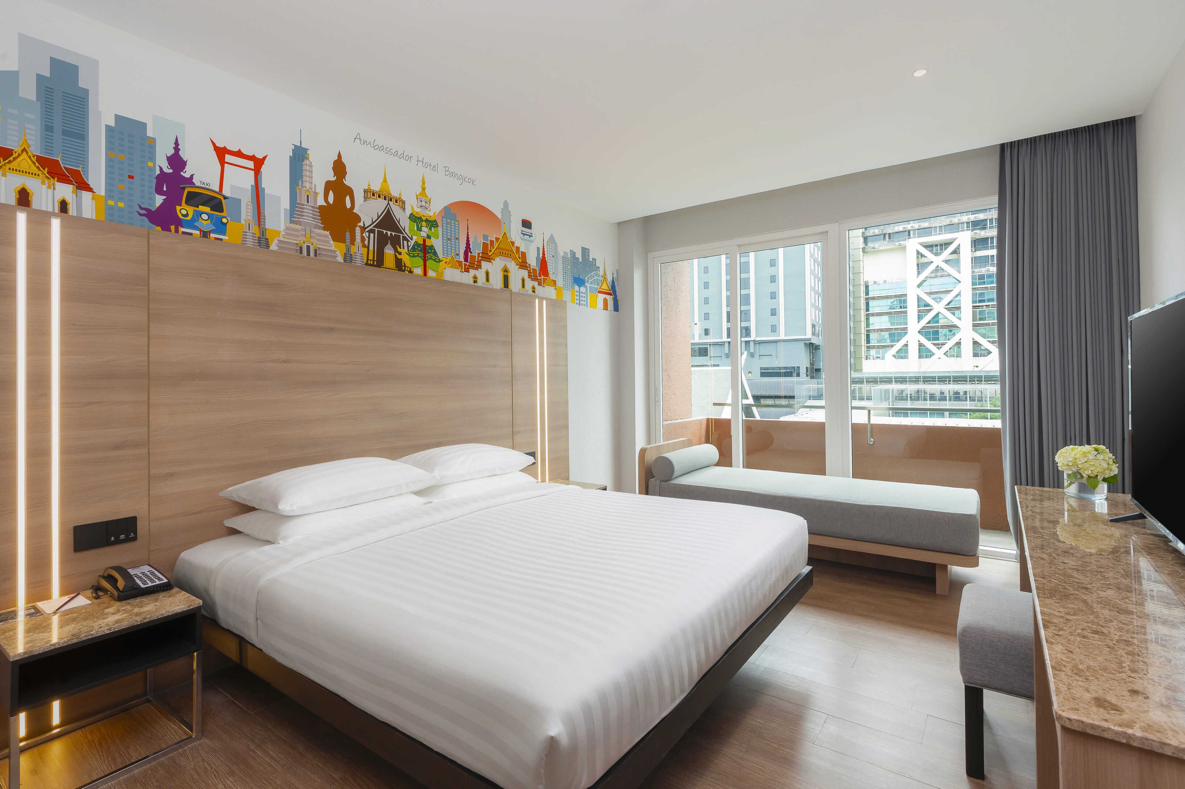 A hotel room with a large bed, a desk, a TV, and a window with a city view.