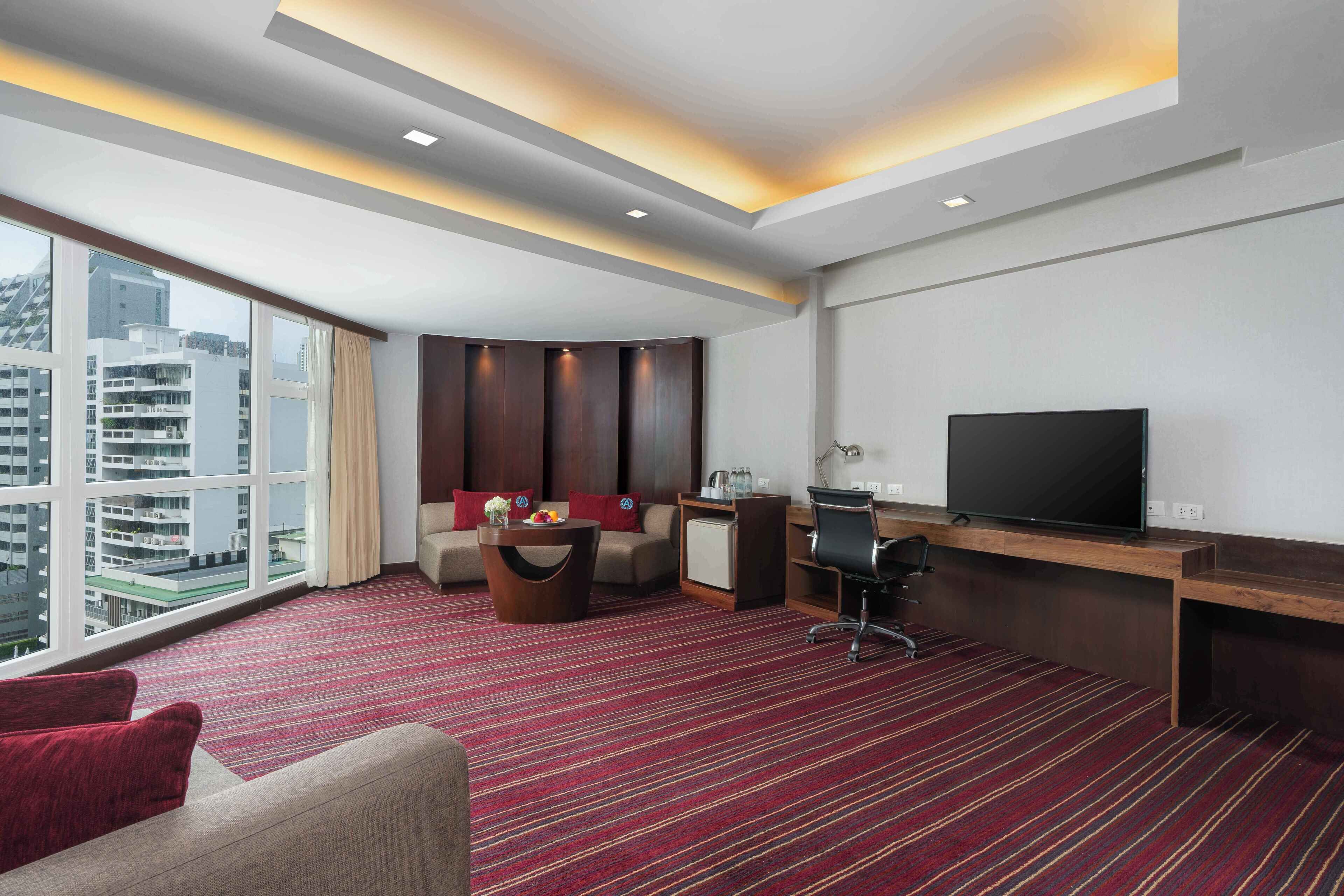 Una habitación de hotel con un ventanal grande, un sofá, un escritorio con televisor y un refrigerador pequeño.