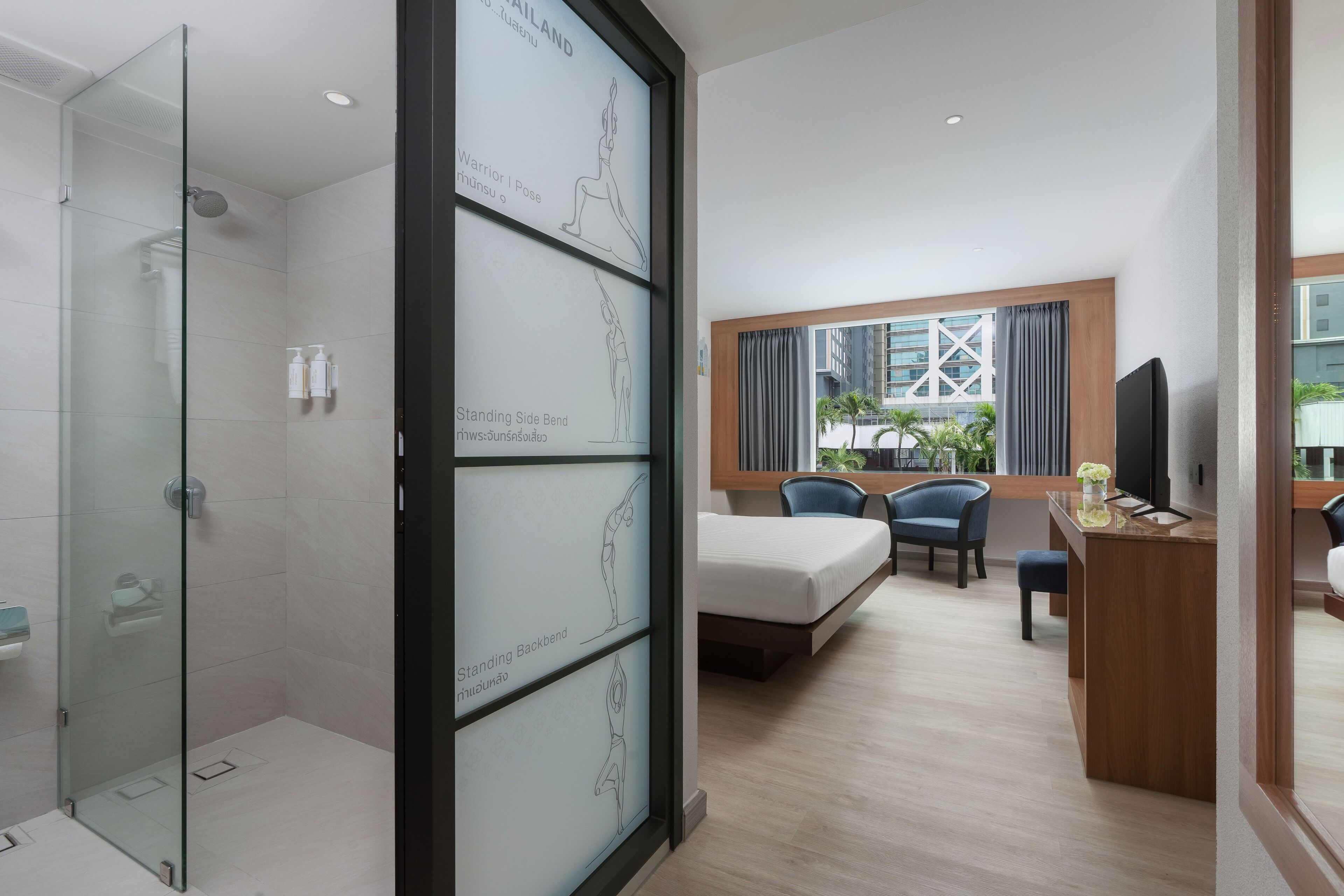 A hotel room with a glass shower enclosure, a bed, a desk with a chair, and a large window with curtains.