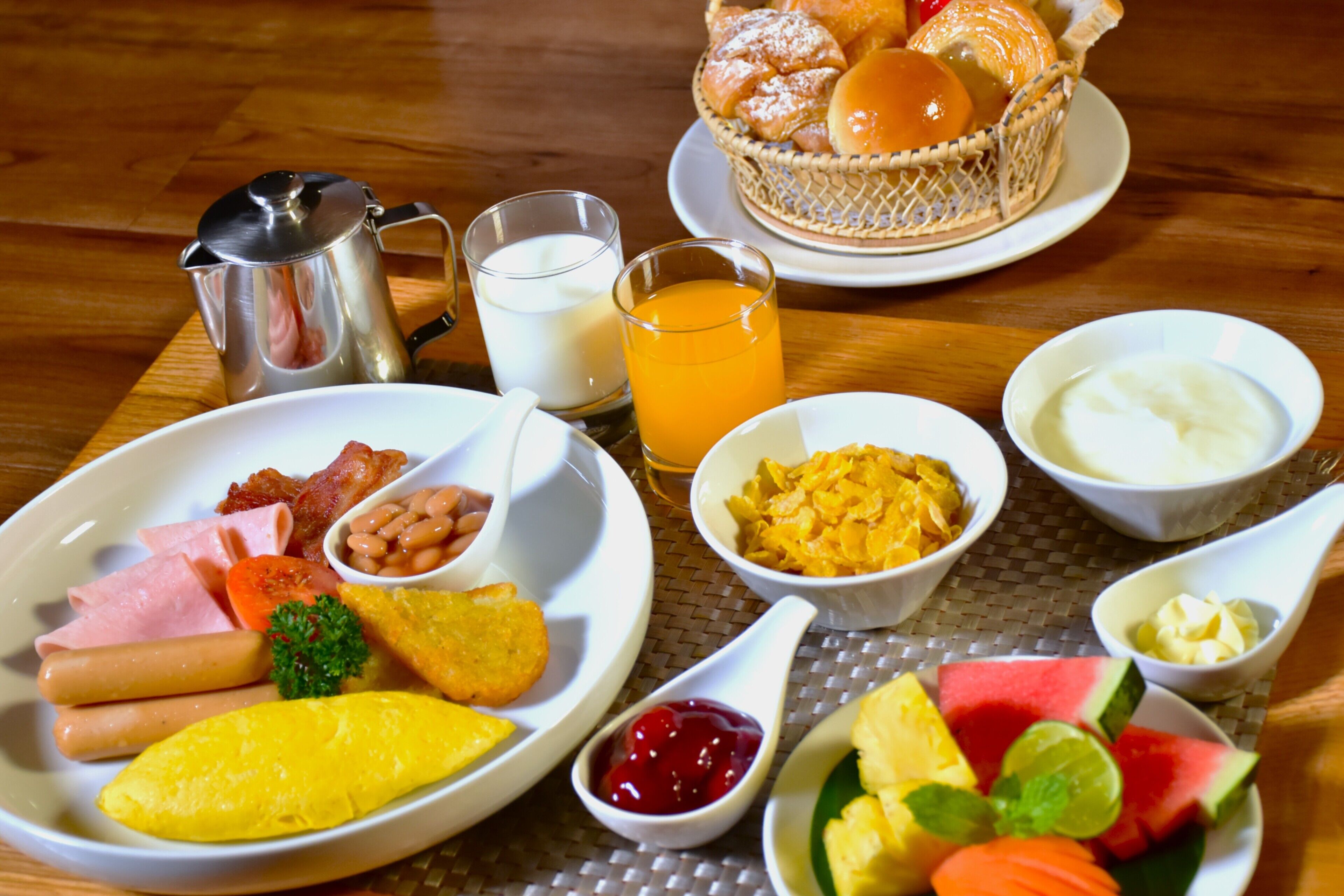 A breakfast table with various dishes including eggs, bacon, ham, beans, and fruits.