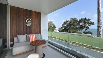 A modern balcony with a sofa, a round table, and a drum. It overlooks a green lawn and a body of water.