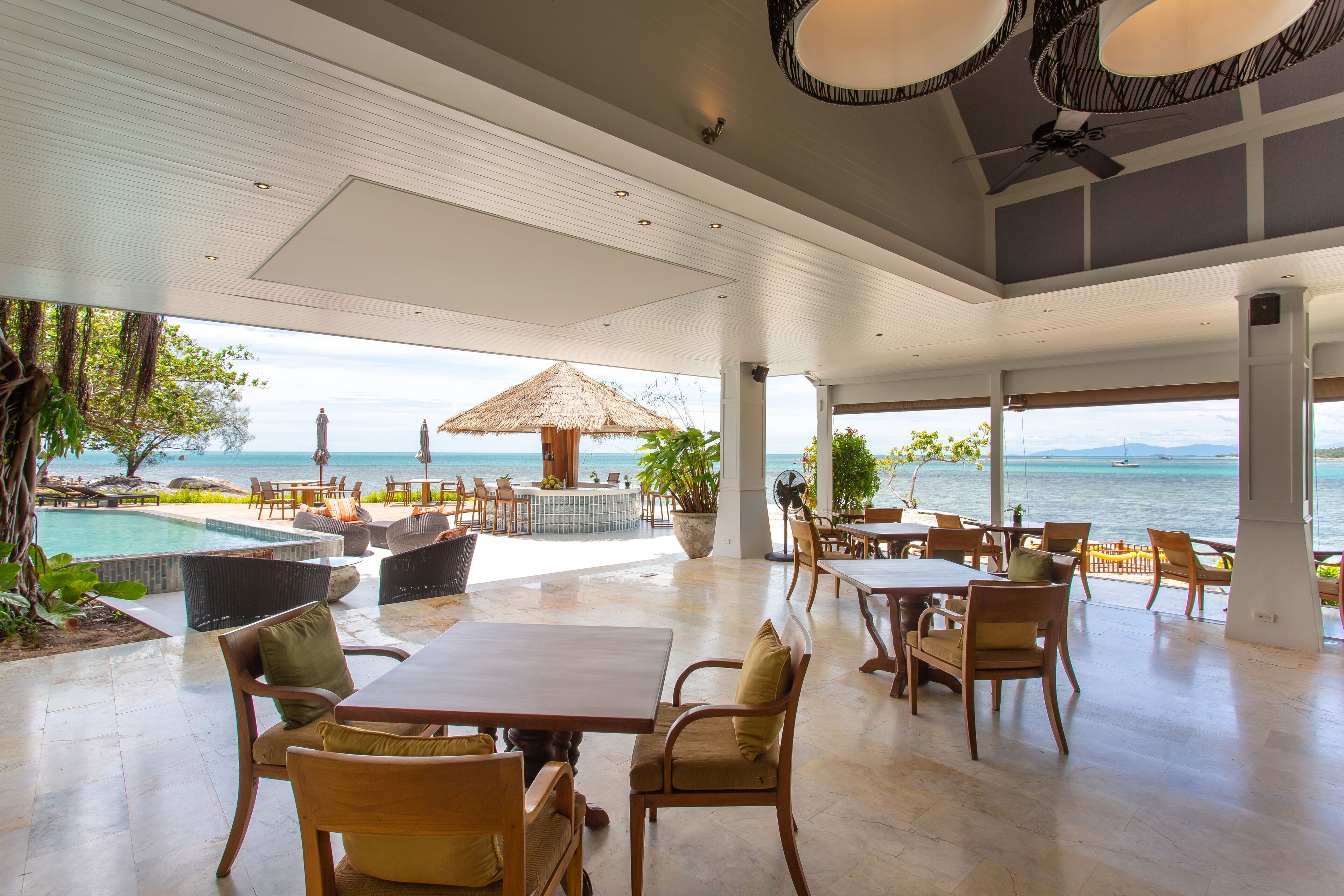 Un vaste espace de détente extérieur avec piscine, tables et chaises, offrant une vue panoramique sur l’océan.