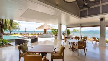 Un vaste espace de détente extérieur avec piscine, tables et chaises, offrant une vue panoramique sur l’océan.