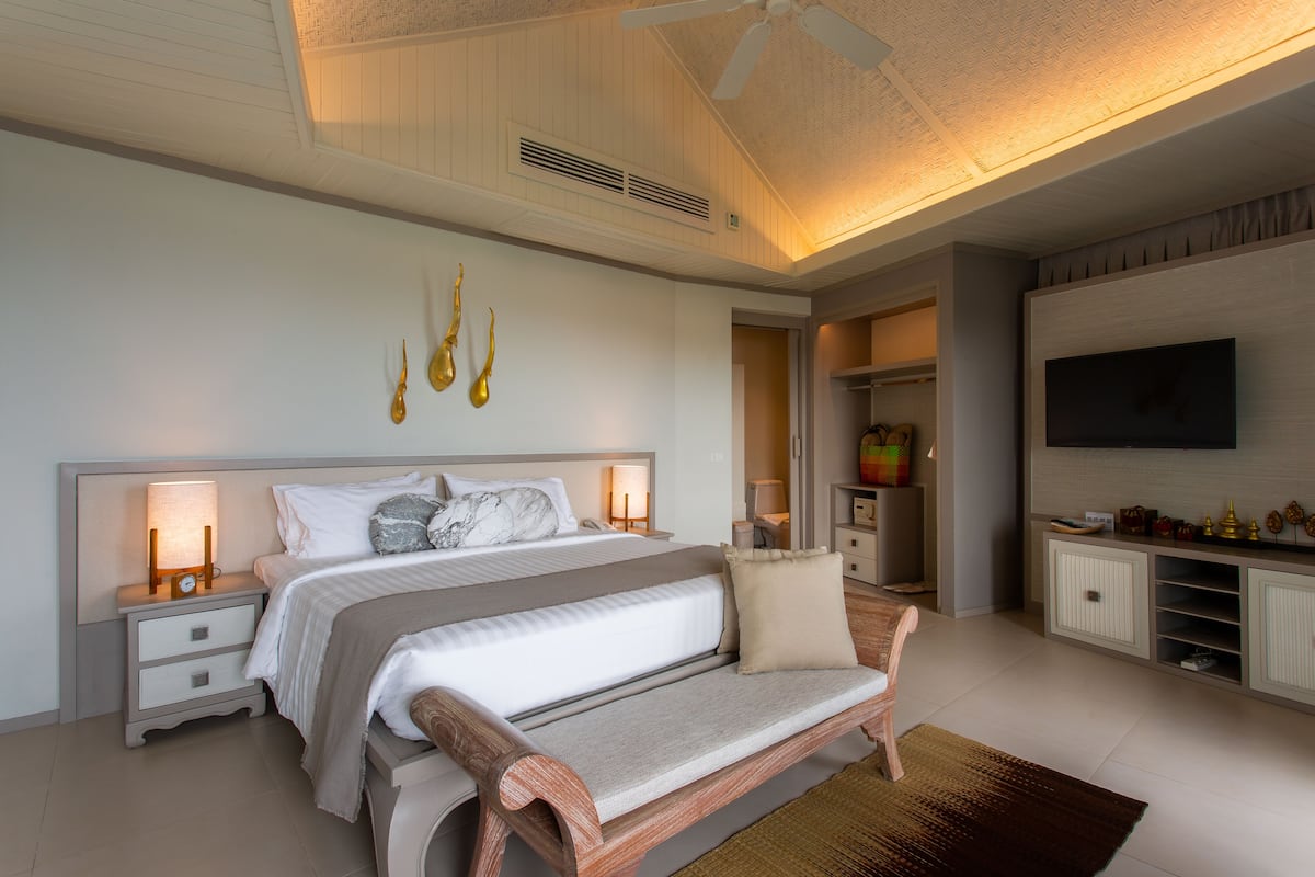 Une chambre à coucher moderne avec un grand lit, des tables de chevet, un banc, une télévision et un dressing.