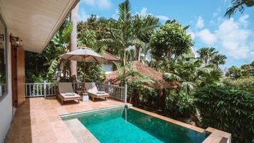 A swimming pool with lounge chairs and a thatched-roof structure surrounded by lush greenery.