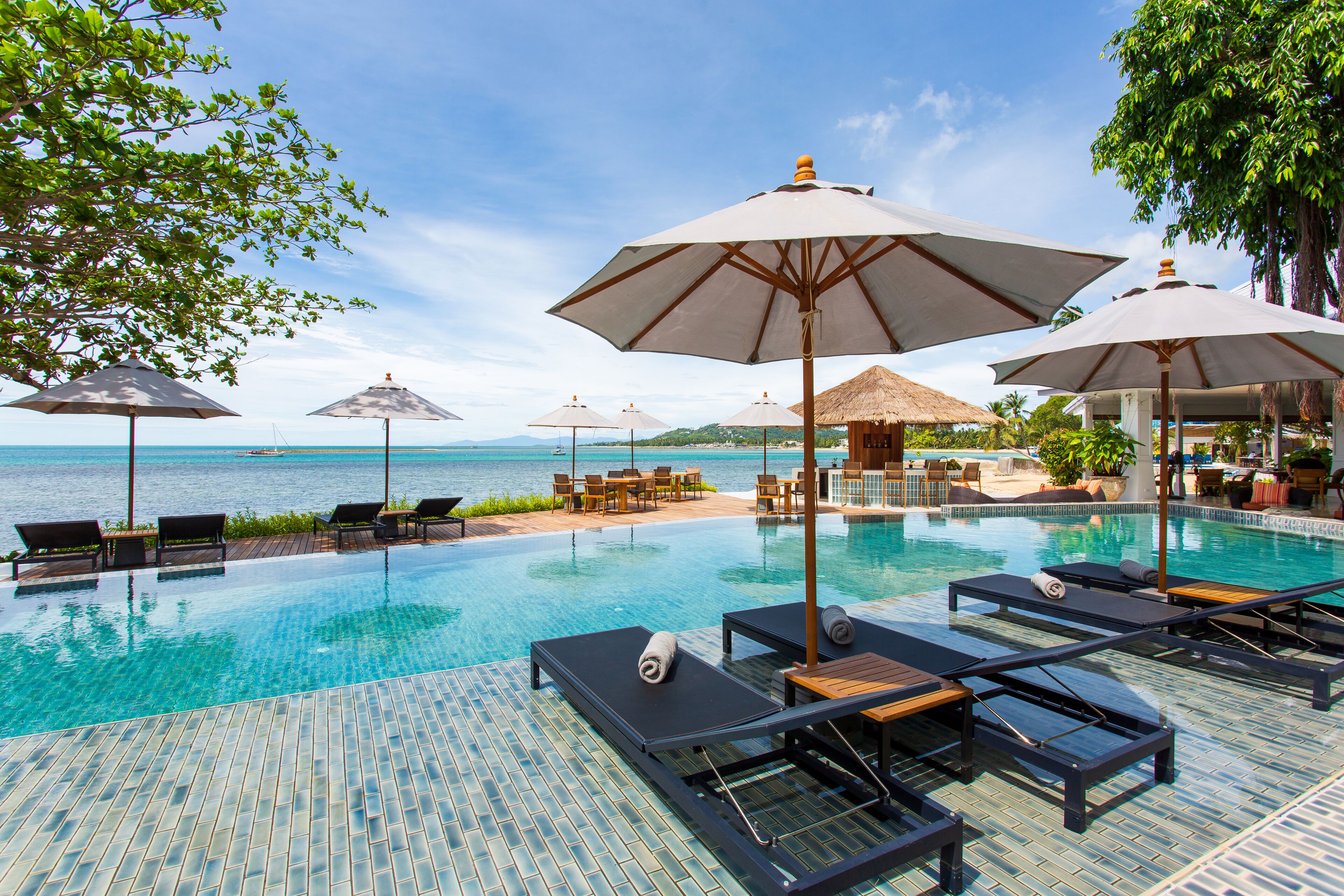 An infinity pool with lounge chairs and umbrellas, overlooking a clear blue sea.