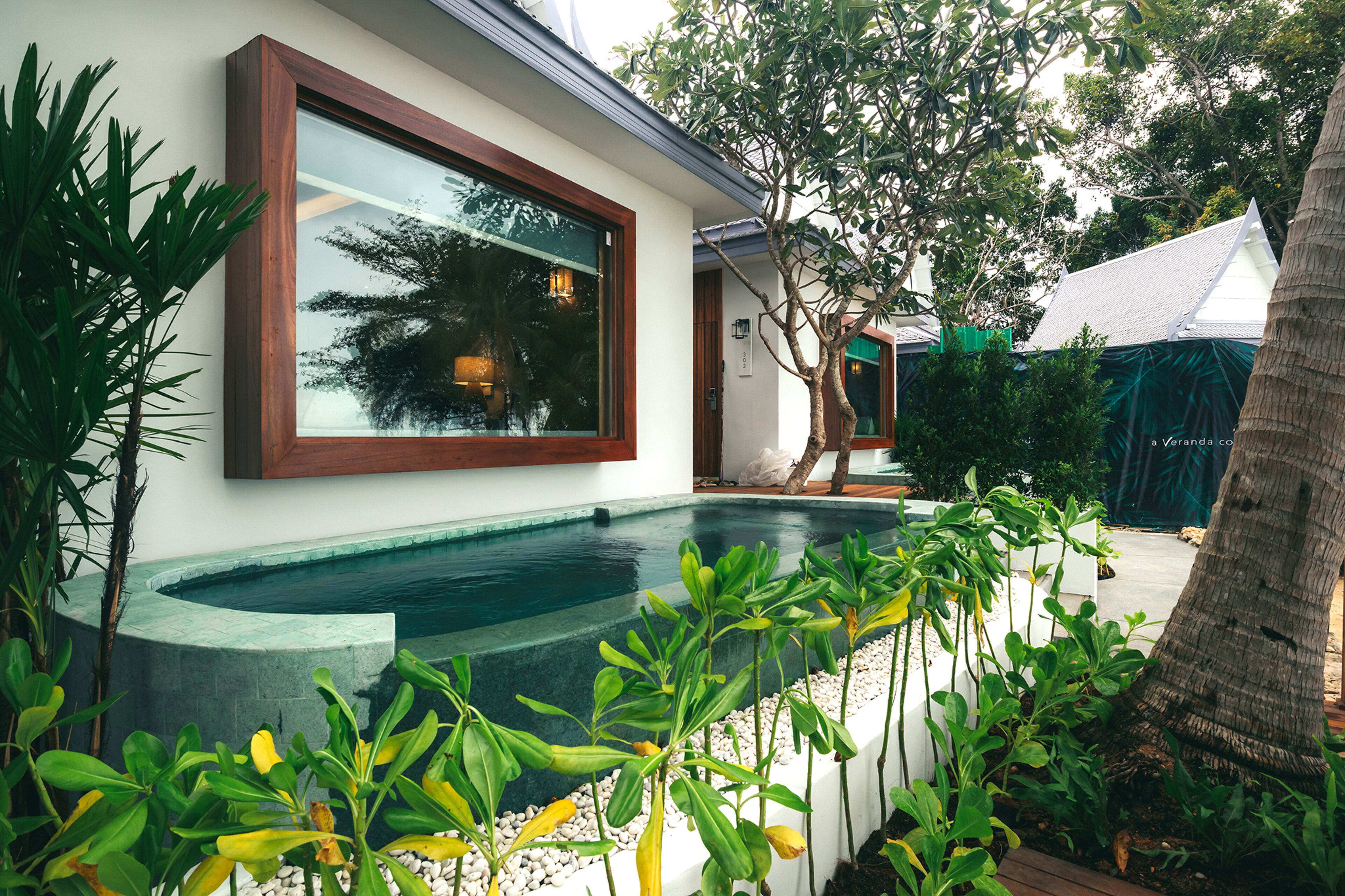 A modern house with a large window, a swimming pool, and lush greenery.