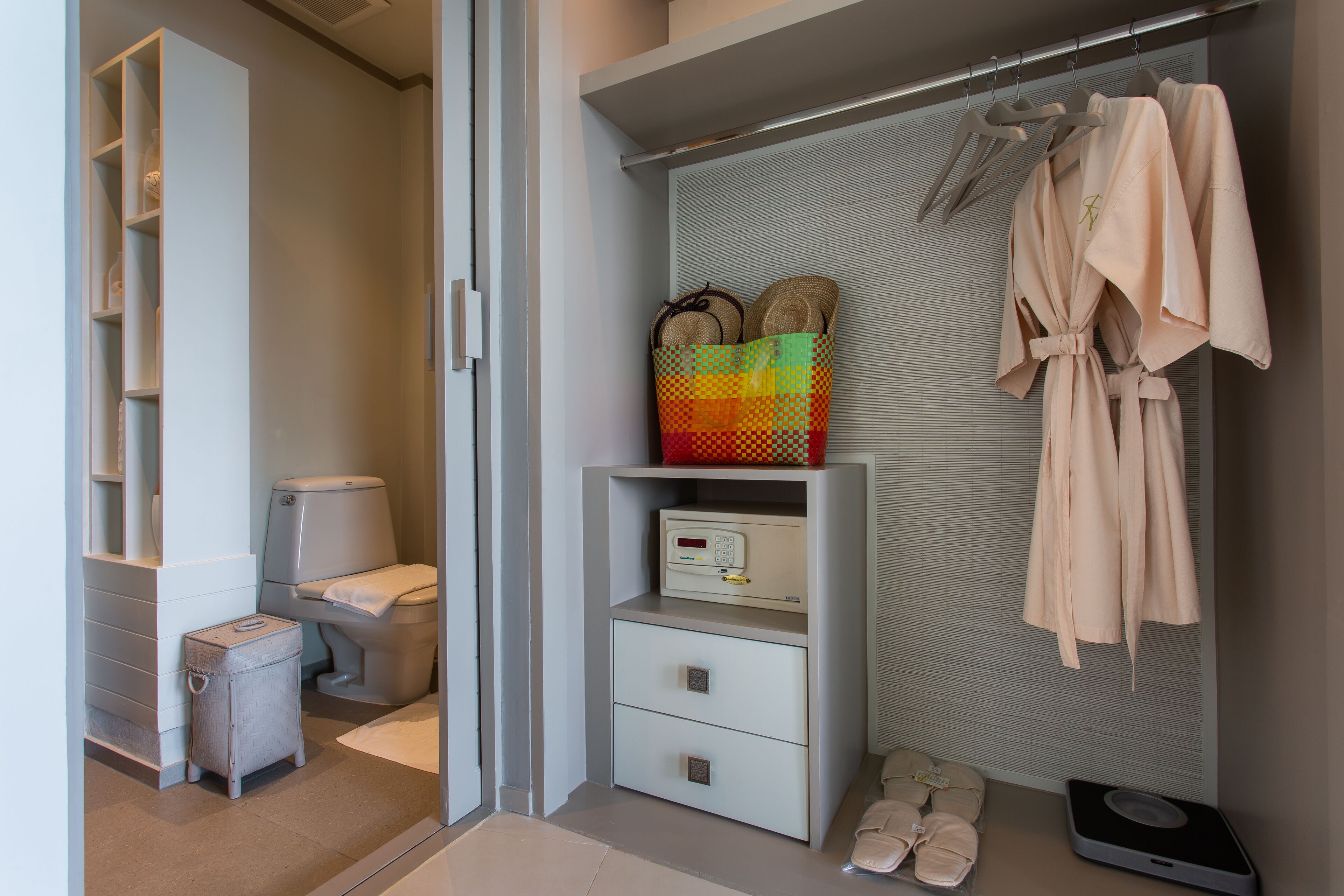 Ein modernes Badezimmer mit Toilette, einem kleinen Nachttisch, einem Stauraum mit Waage und einem Bademantel an einem Gestell.