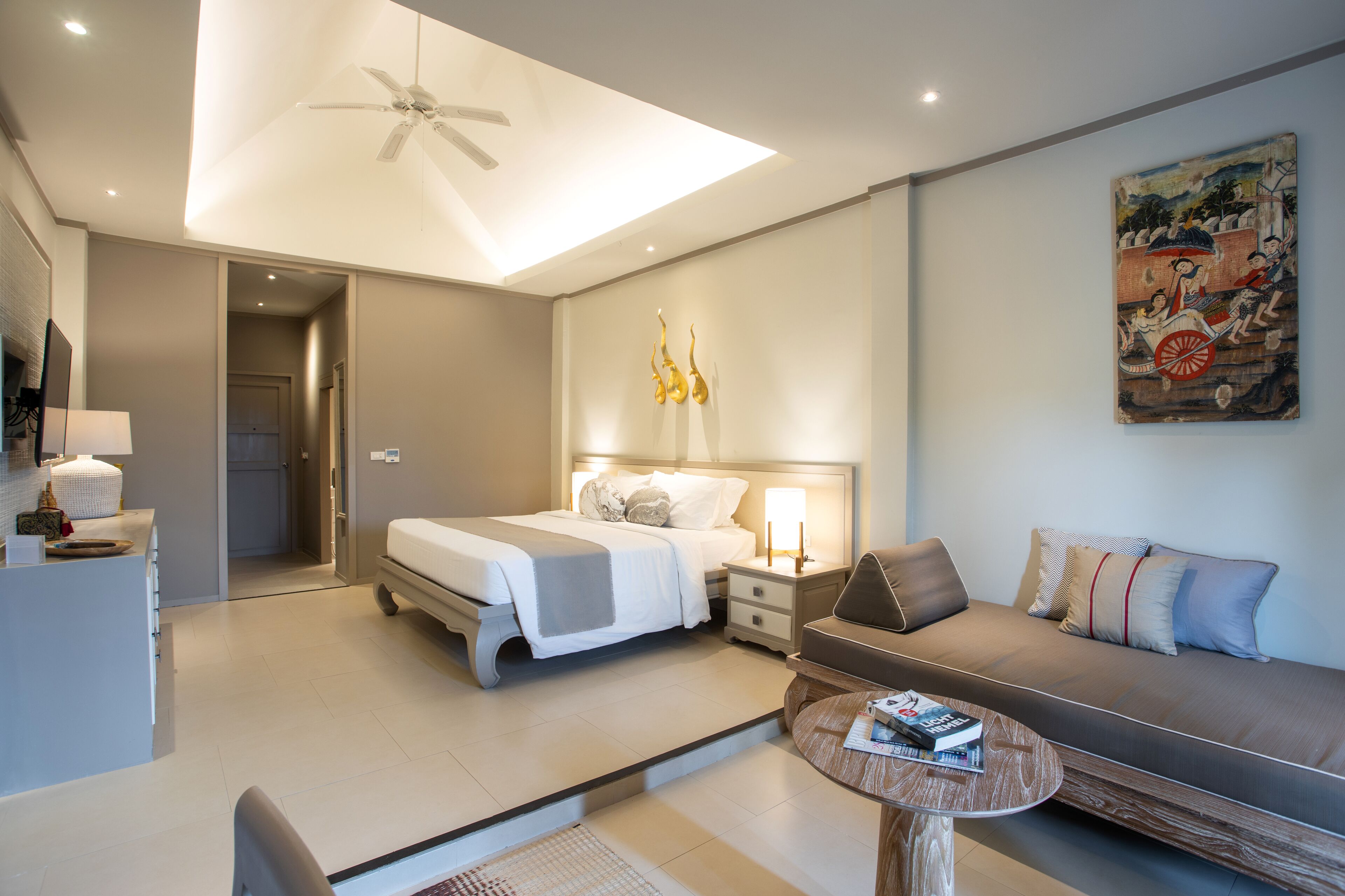 A modern hotel room with a bed, a sofa, a small table, and a ceiling fan.