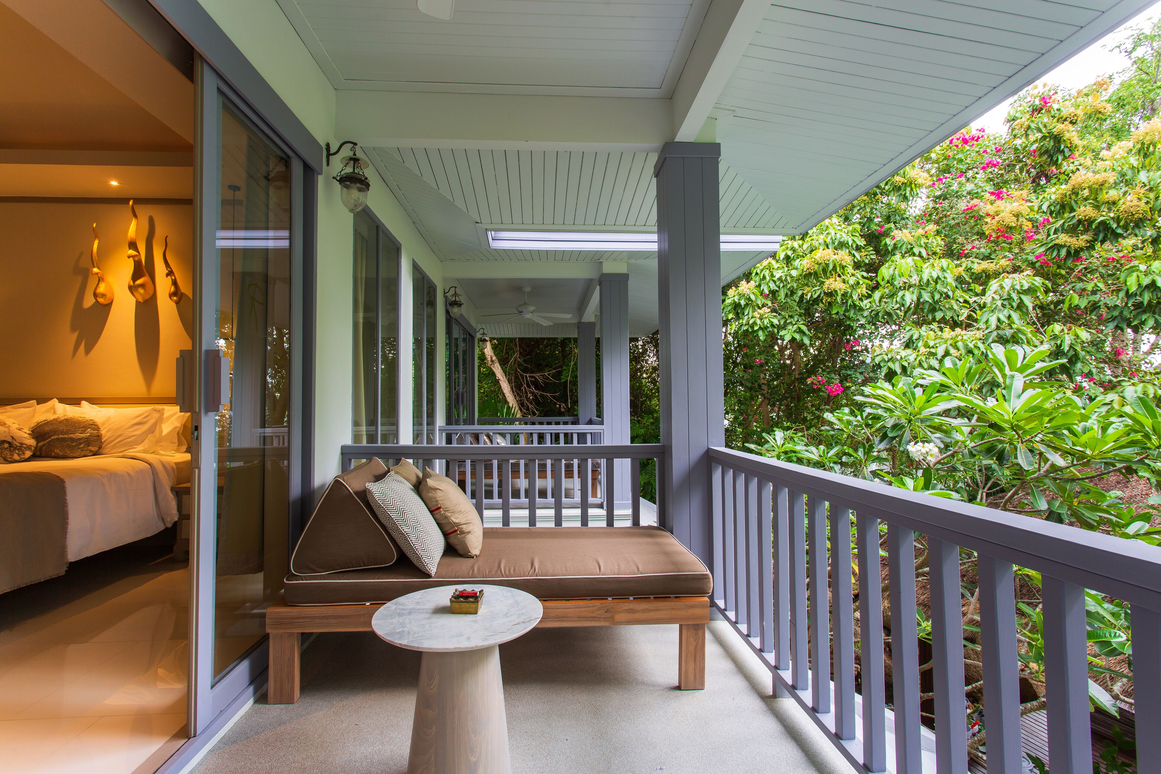 Un balcon avec un canapé et une table, un lit avec des oreillers et une vue sur une végétation luxuriante.