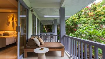 Un balcon avec un canapé et une table, un lit avec des oreillers et une vue sur une végétation luxuriante.