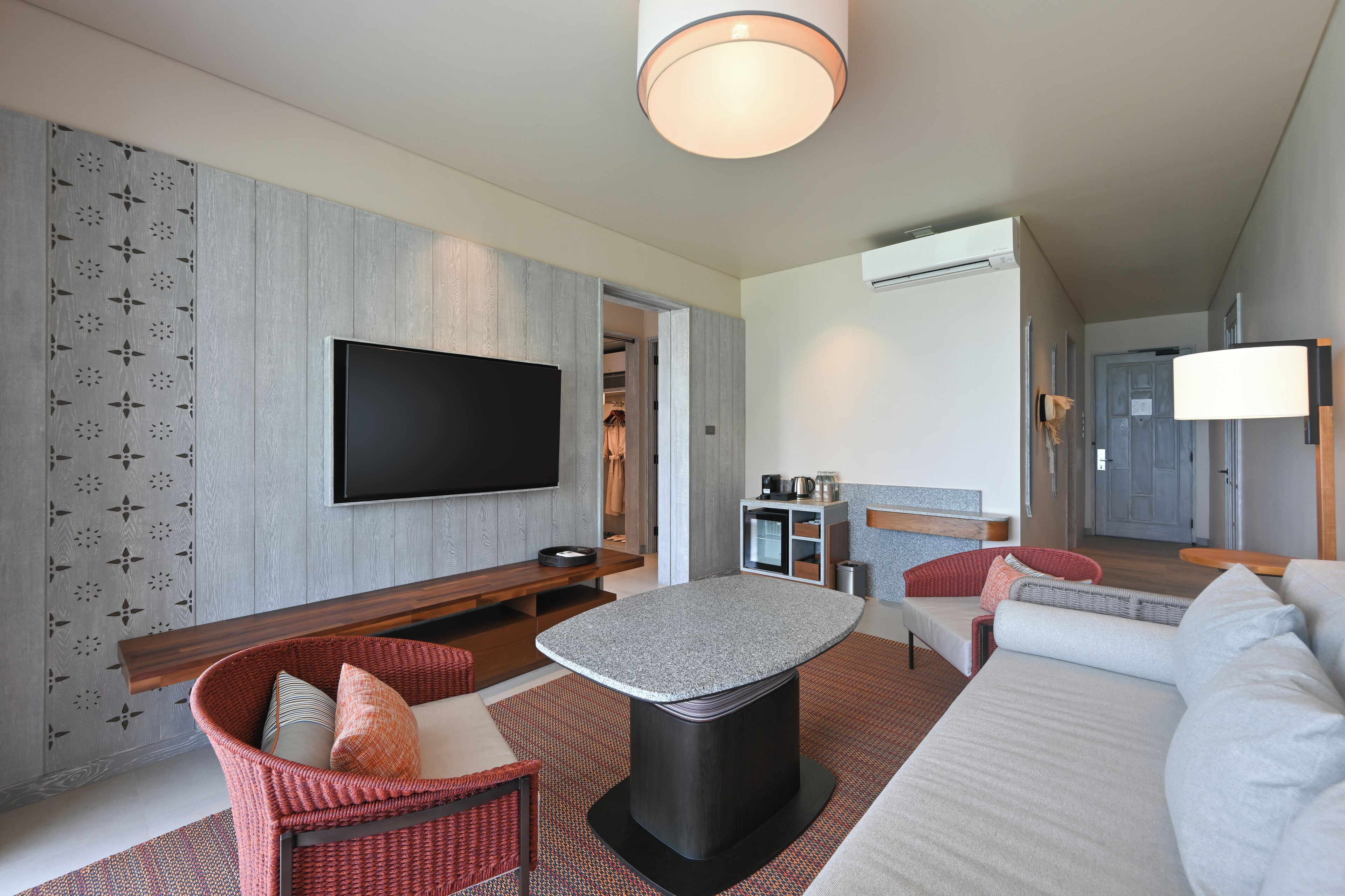 A modern living room with a flat-screen TV, a round coffee table, a sofa, and a wicker chair.