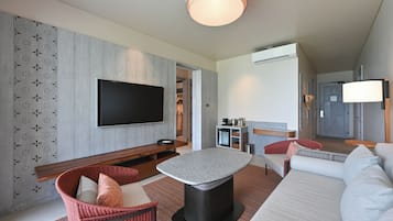 A modern living room with a flat-screen TV, a round coffee table, a sofa, and a wicker chair.