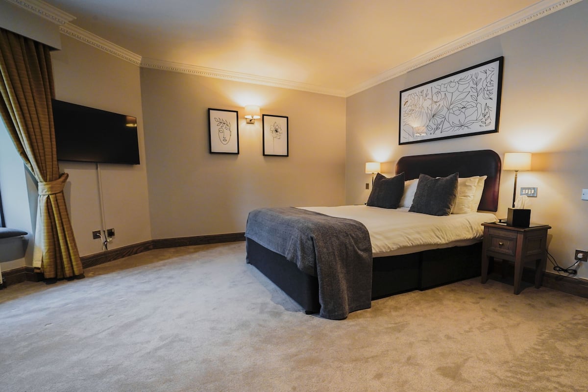 A neatly arranged bedroom with a bed, bedside lamps, a flat-screen TV, and framed artwork on the wall.