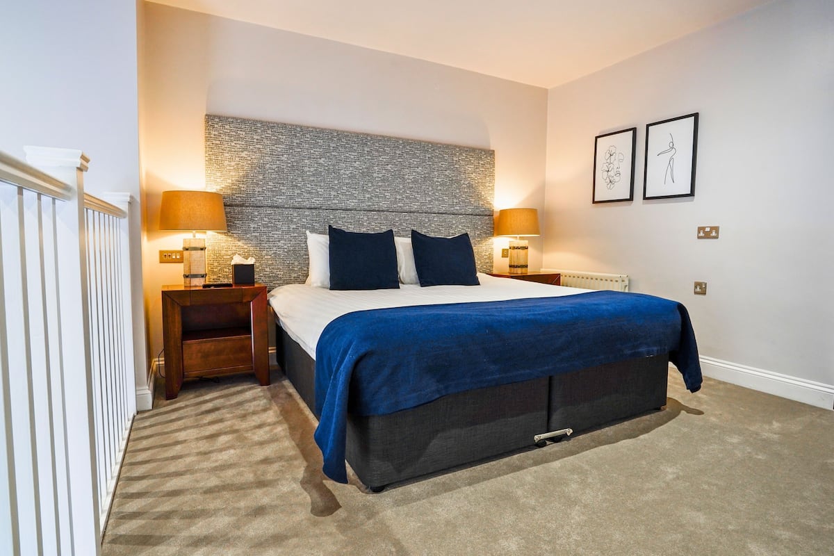 A modern bedroom with a large bed, two bedside tables, a headboard with a textured pattern, and two wall-mounted lamps.