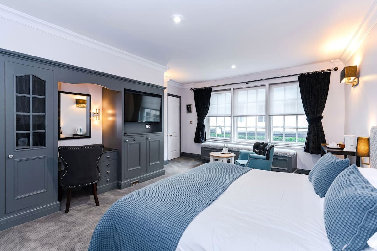 A hotel room with a large bed, a desk with a chair, a TV, and a window with curtains.