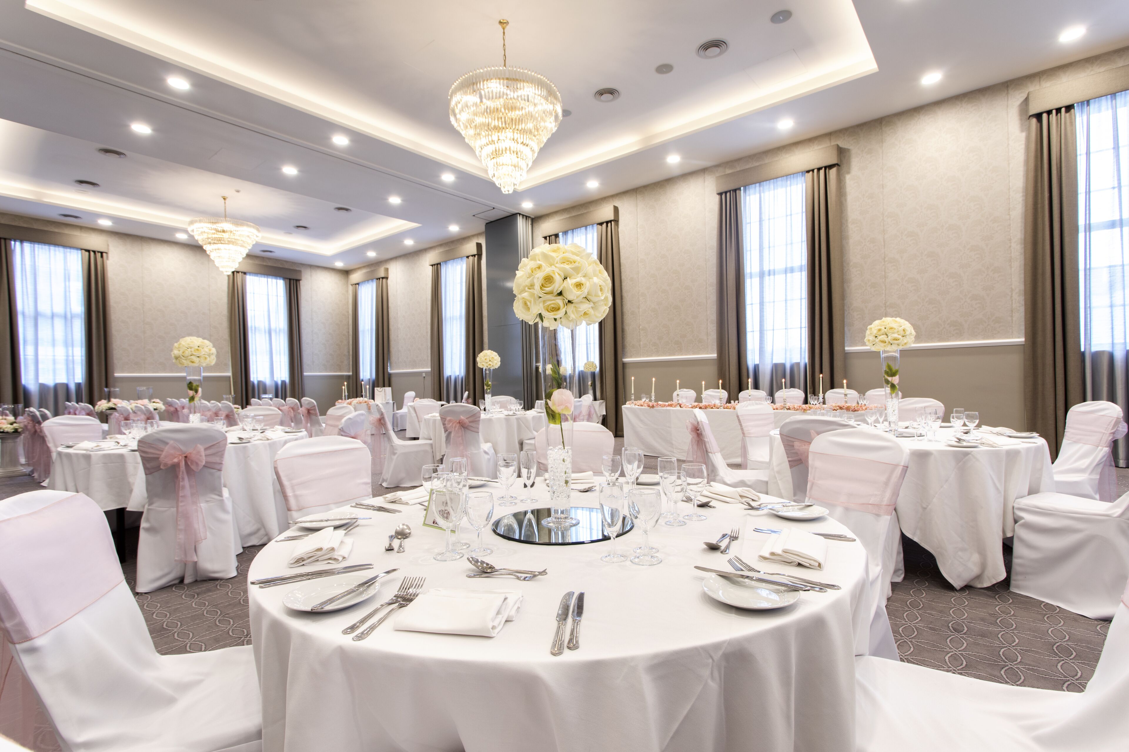 A banquet hall with round tables set for dining, chandeliers, and floral centerpieces.