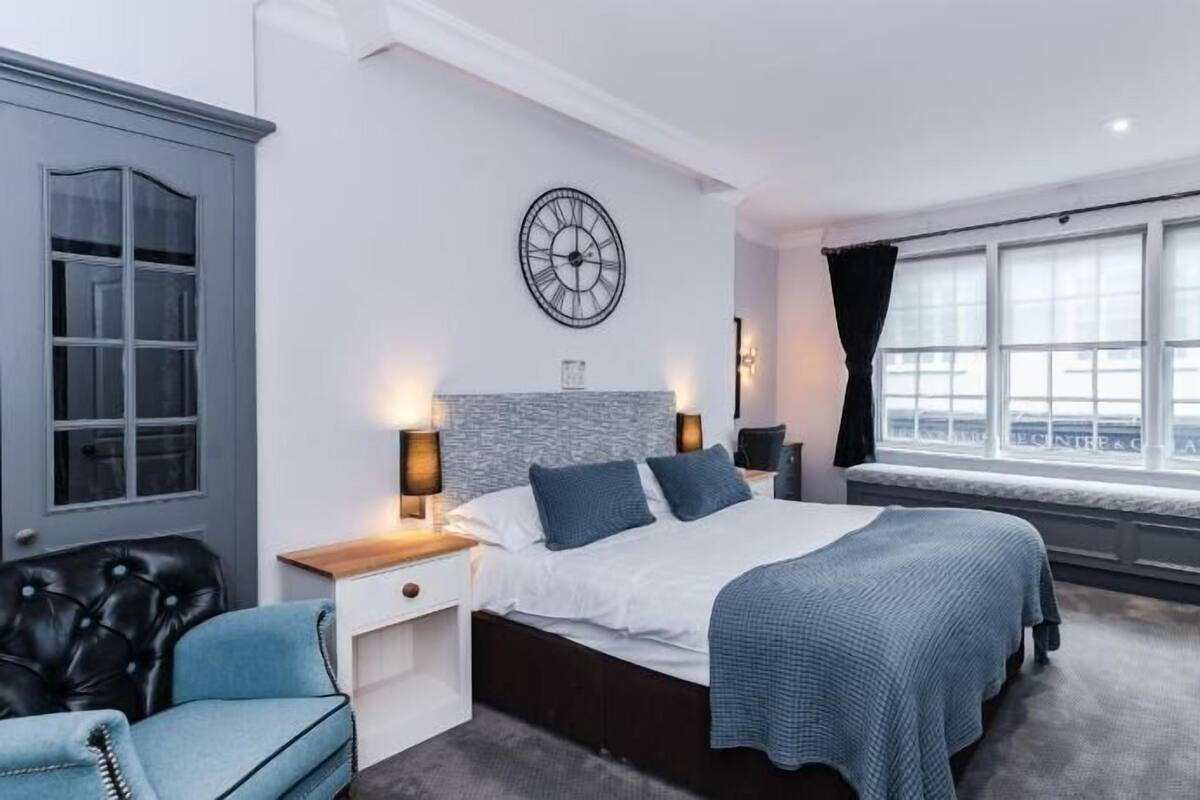 A modern bedroom with a large bed, a clock on the wall, and a view of the city through the window.