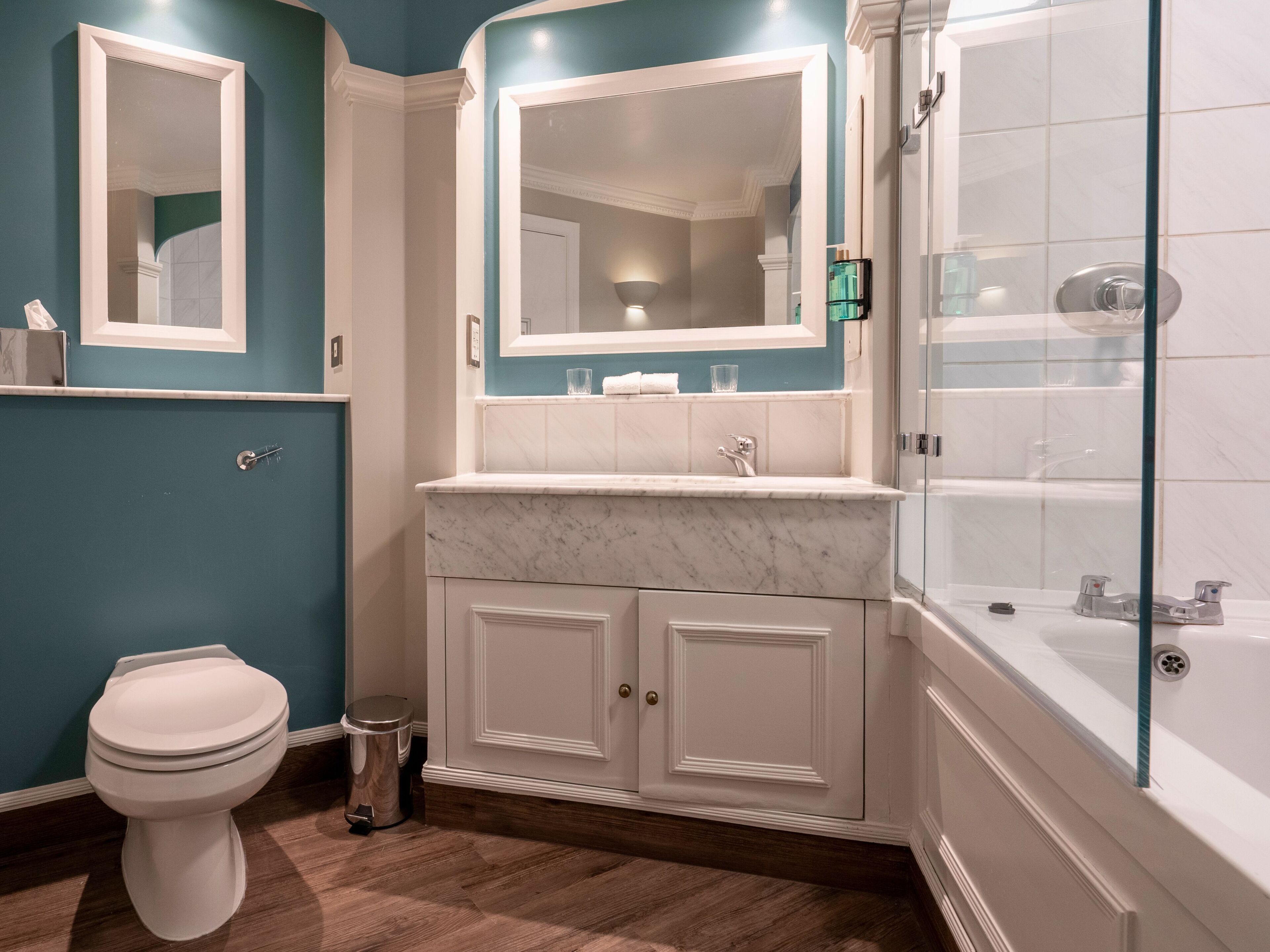 A bathroom with a toilet, a sink with a mirror, a shower area, and a cabinet.