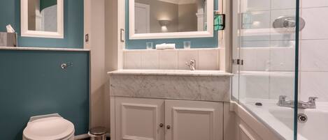 A bathroom with a toilet, a sink with a mirror, a shower area, and a cabinet.
