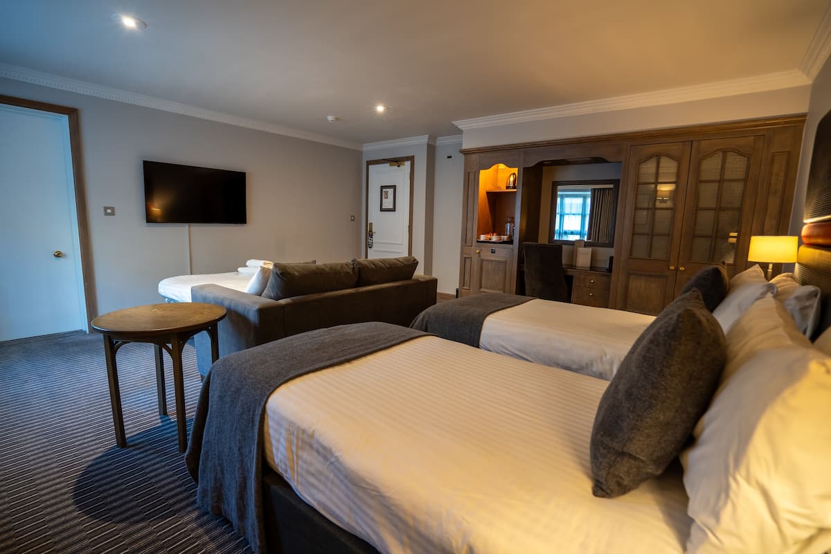 A hotel room with two beds, a sofa, a TV, and a small table.