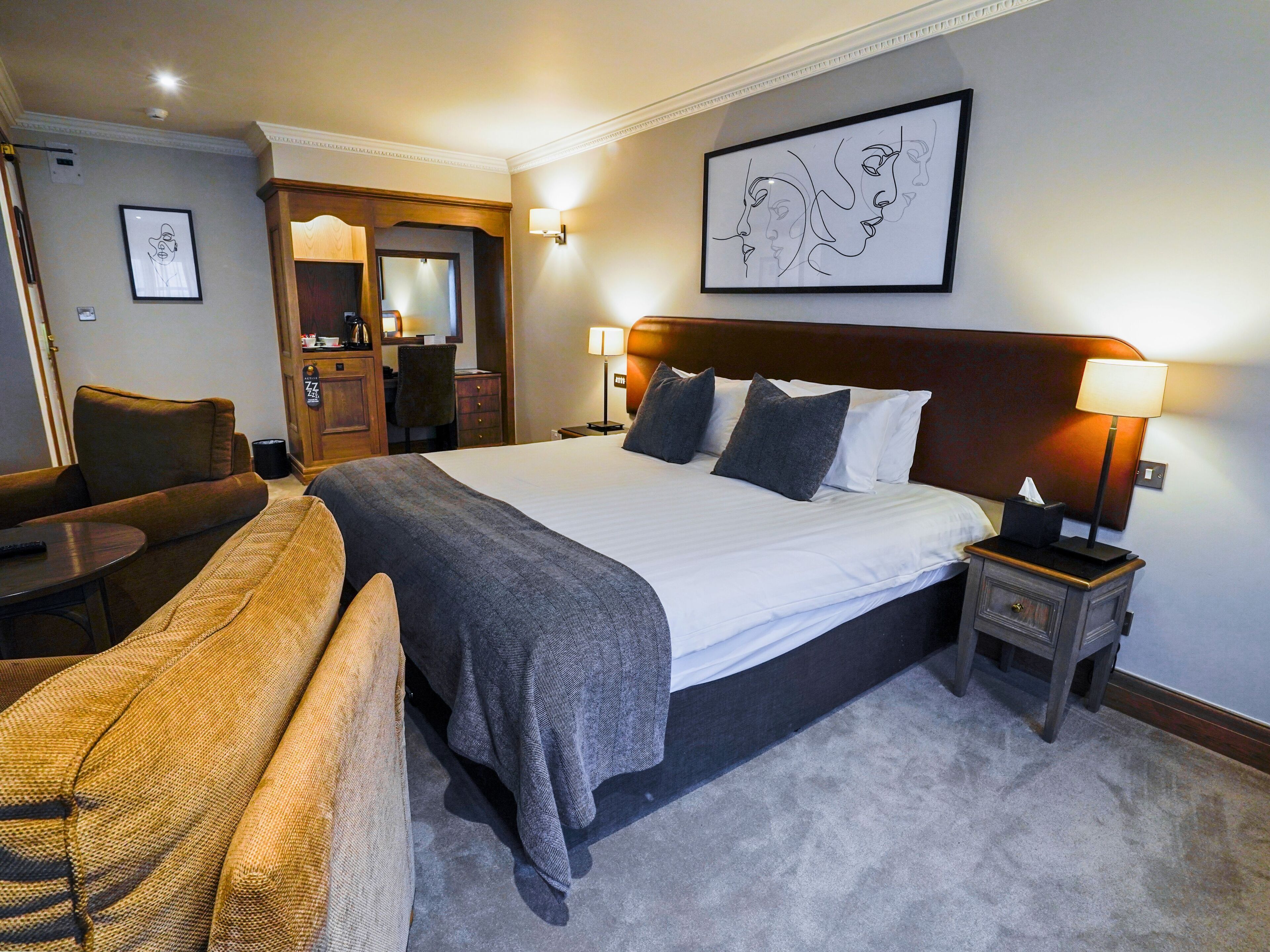 A hotel room with a large bed, a desk, a chair, and a sofa.